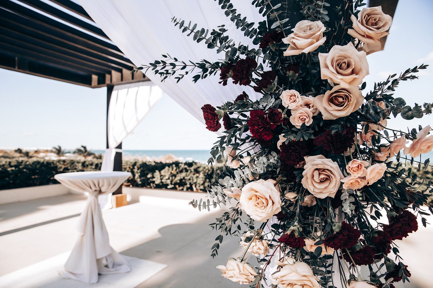 A large floral arrangement with roses, greenery, and other flowers, displayed on a table with a view of the outdoors.