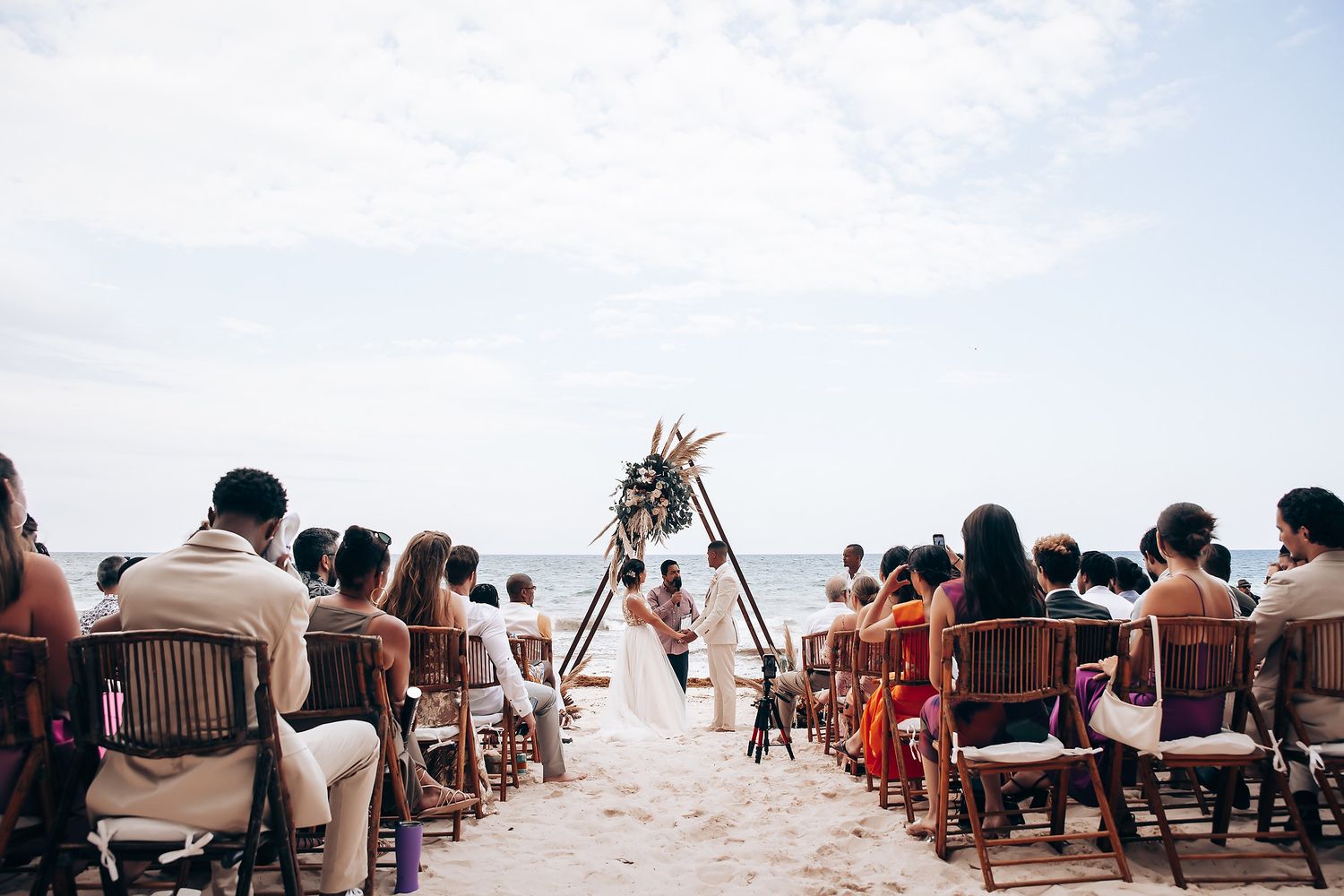 Guests seated in rows at an outdoor beachfront wedding ceremony.