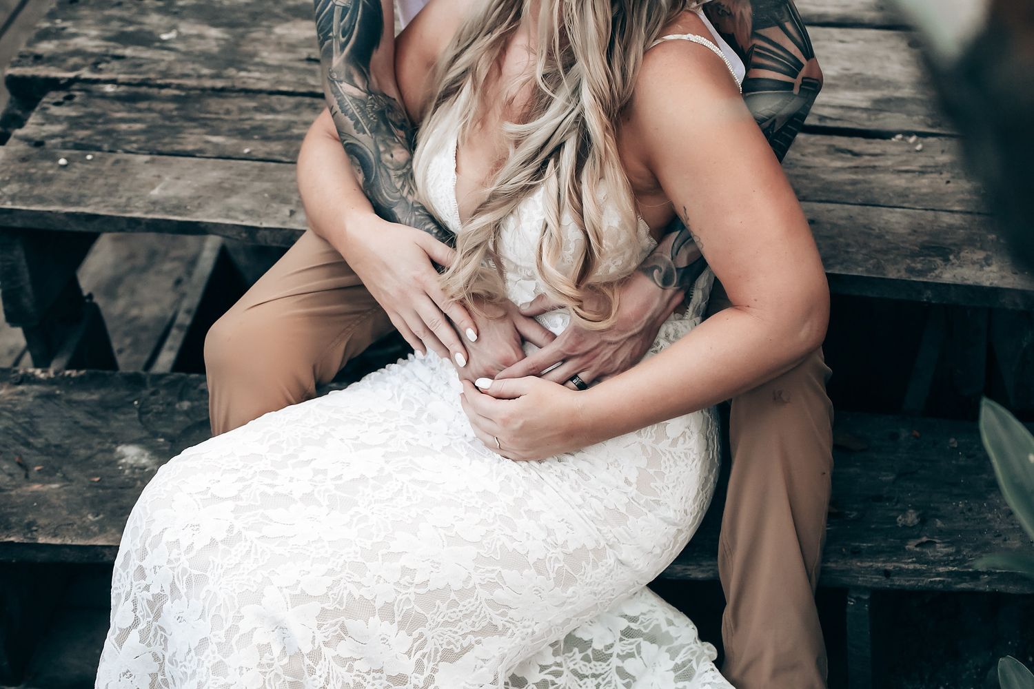 A white wedding dress with intricate lace detailing is showcased in natural outdoor lighting.
