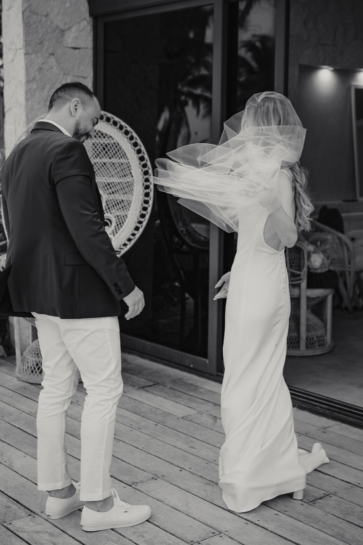 Black and white photo of bride and groom walking on wooden deck, veil blowing in wind.
