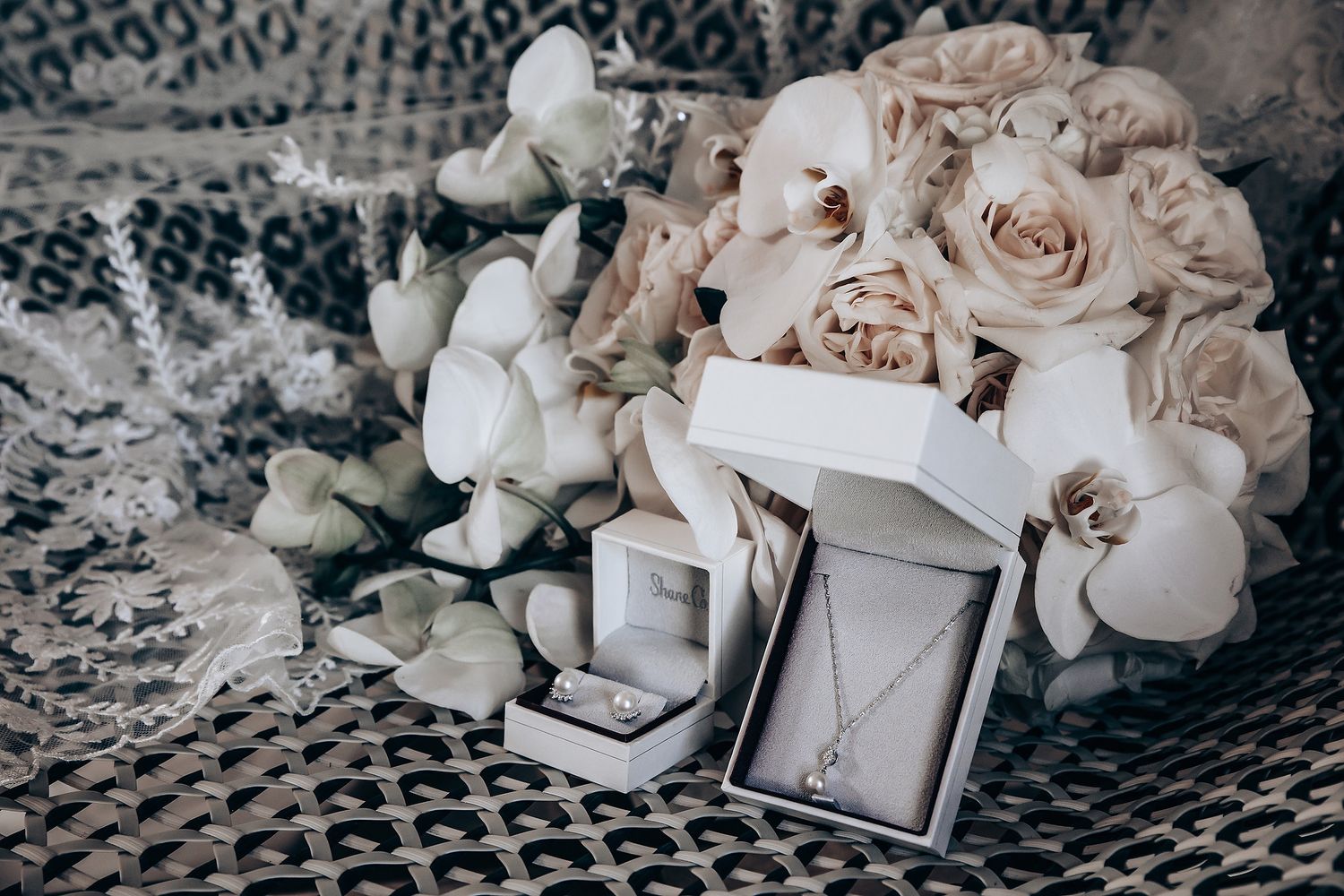 Wedding rings in white boxes displayed with elegant rose bouquet on textured fabric.