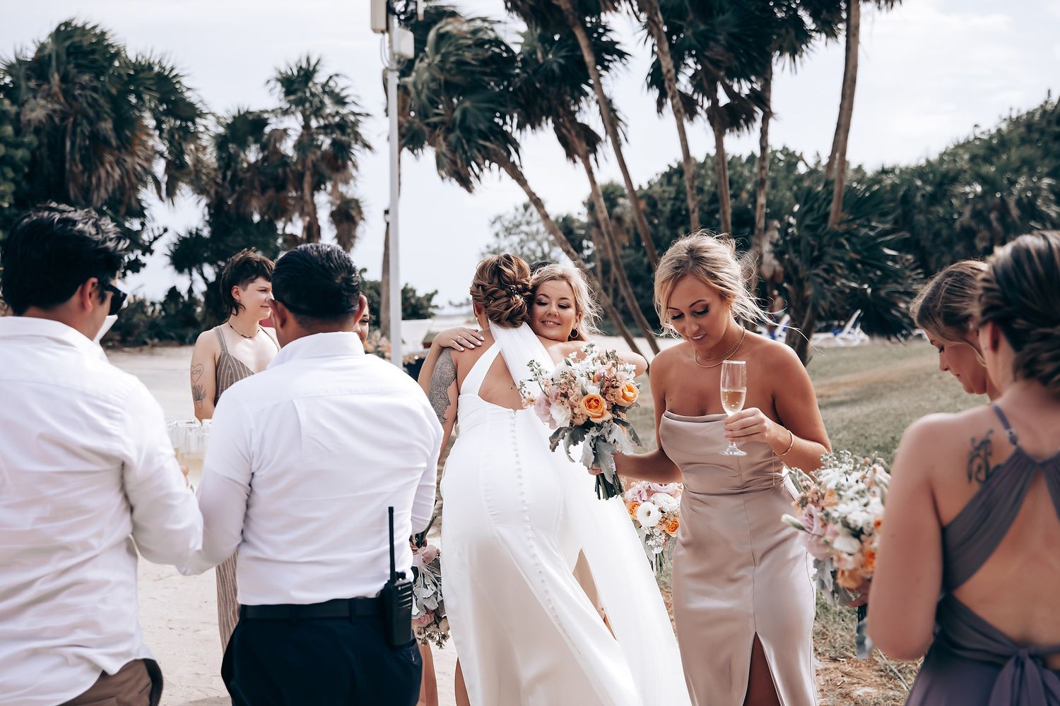 Wedding party laughs and celebrates together outdoors under palm trees at tropical destination ceremony.