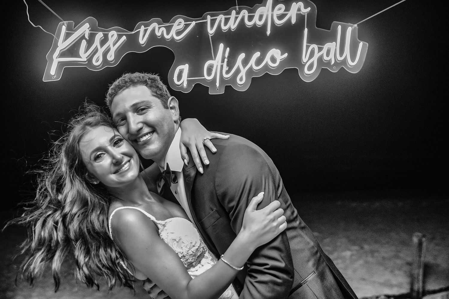 A neon sign reading 'Kiss me under a disco ball' glows against a dark background.