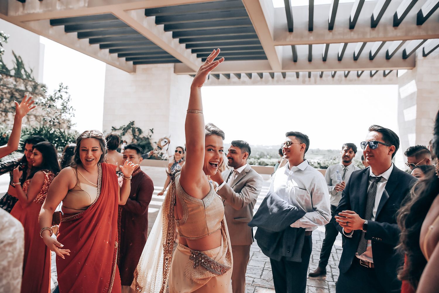 Wedding guests dance and celebrate together under a white pergola during a lively outdoor reception party.