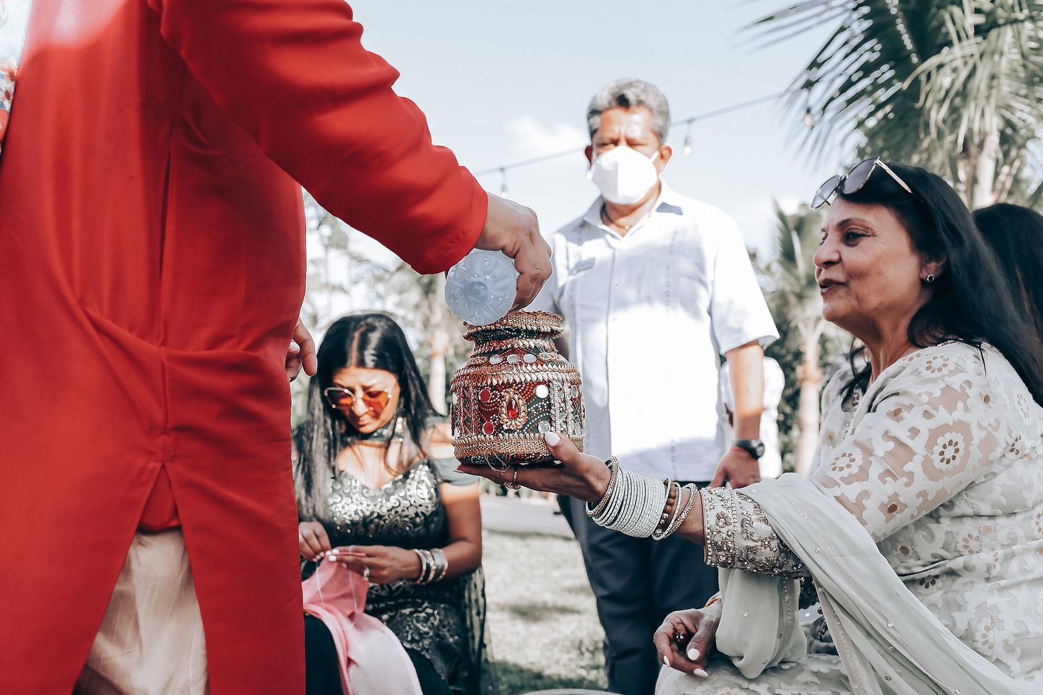 Outdoor wedding reception gathering with guests wearing red and white clothing against a bright sky background.