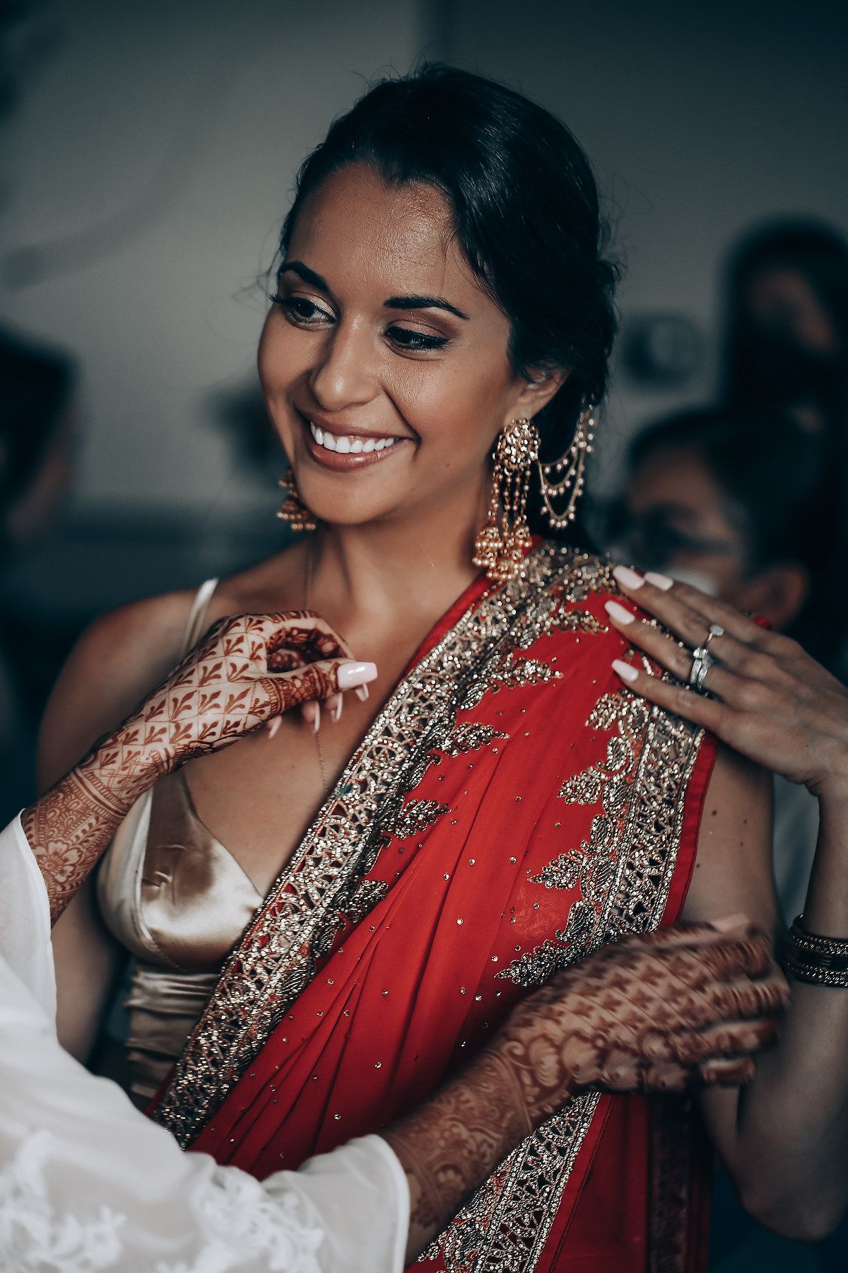 A series of photos showing a bride in a traditional red and gold Indian wedding sari getting ready for her ceremony.