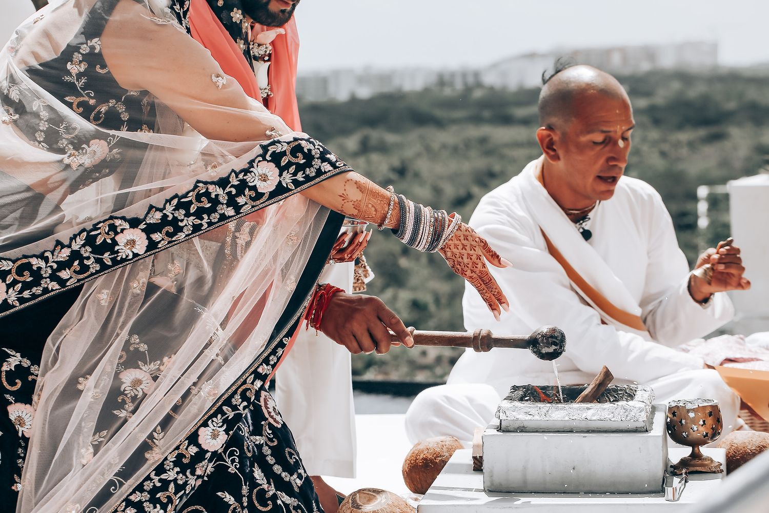 Traditional Indian ceremony participants perform a ritual with offerings and sacred items on an outdoor terrace.
