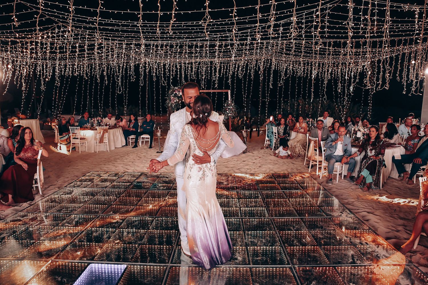 A wedding ceremony setup with rustic wooden chairs and floral arrangements in an outdoor garden setting at sunset.