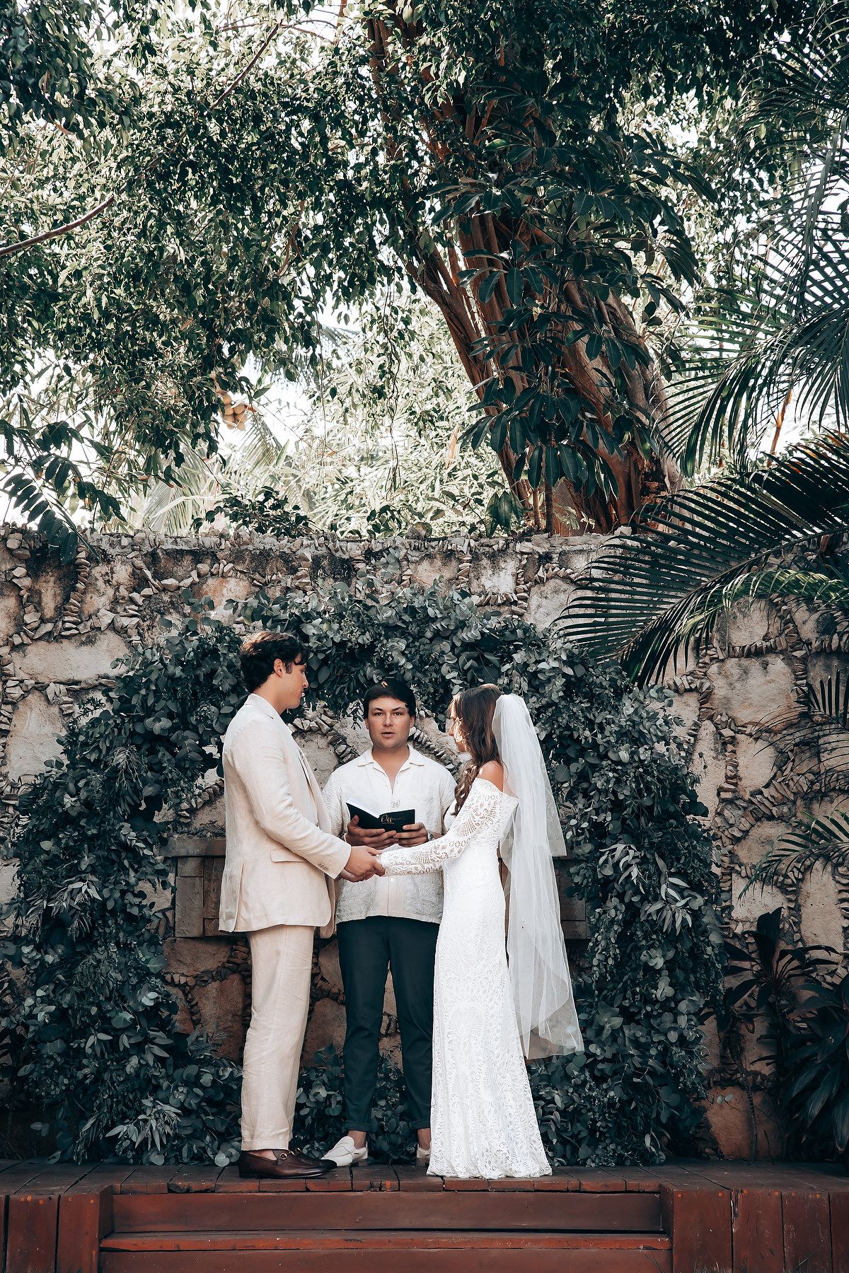 Wedding ceremony preparations in a garden setting with white decor and tropical foliage.