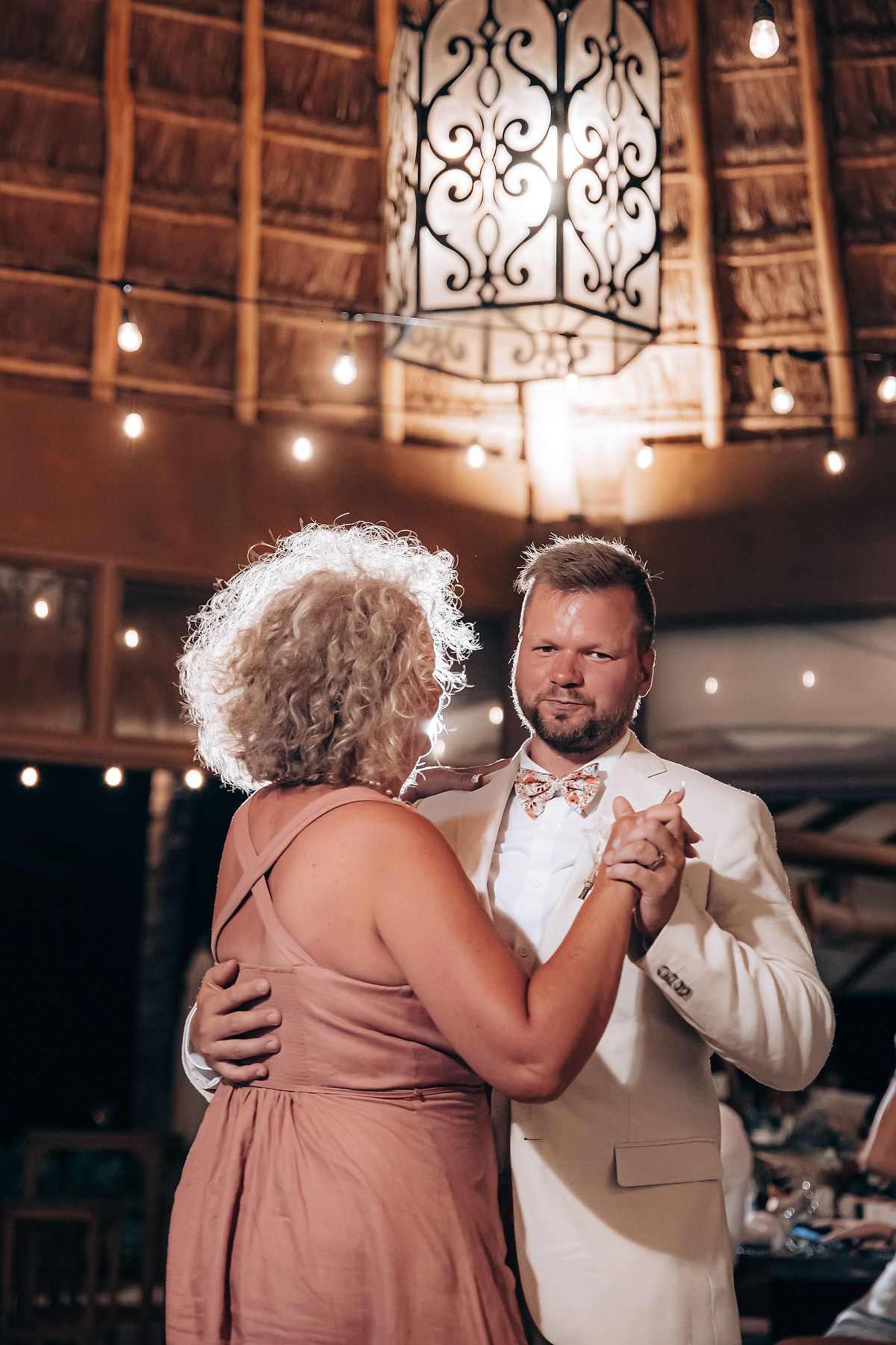 A couple shares a romantic dance moment under decorative lighting at an indoor venue with rustic decor.