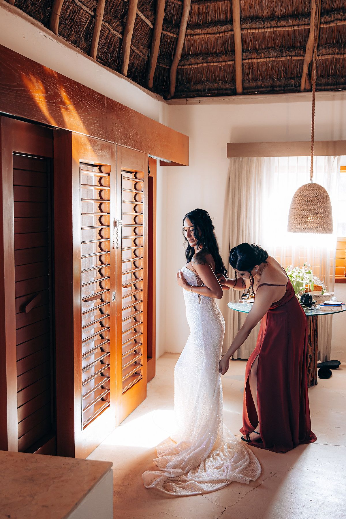 Wedding dress preparations in a tropical resort room with wooden shutters and natural lighting.