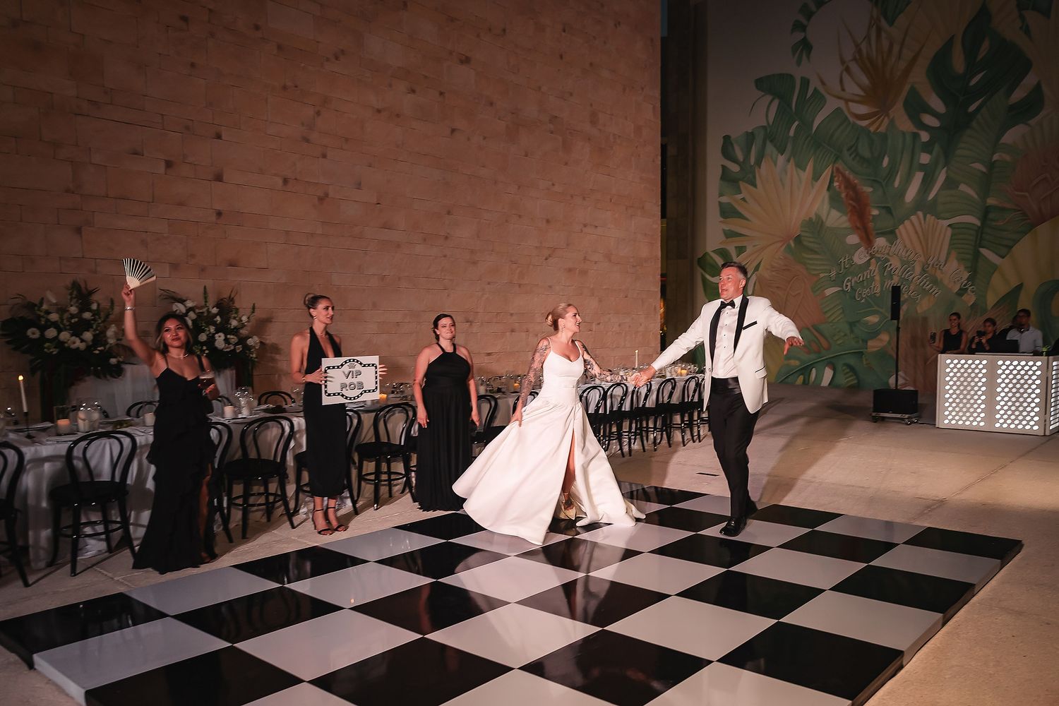 Couple dancing on black and white checkered floor with tropical wall mural in background.