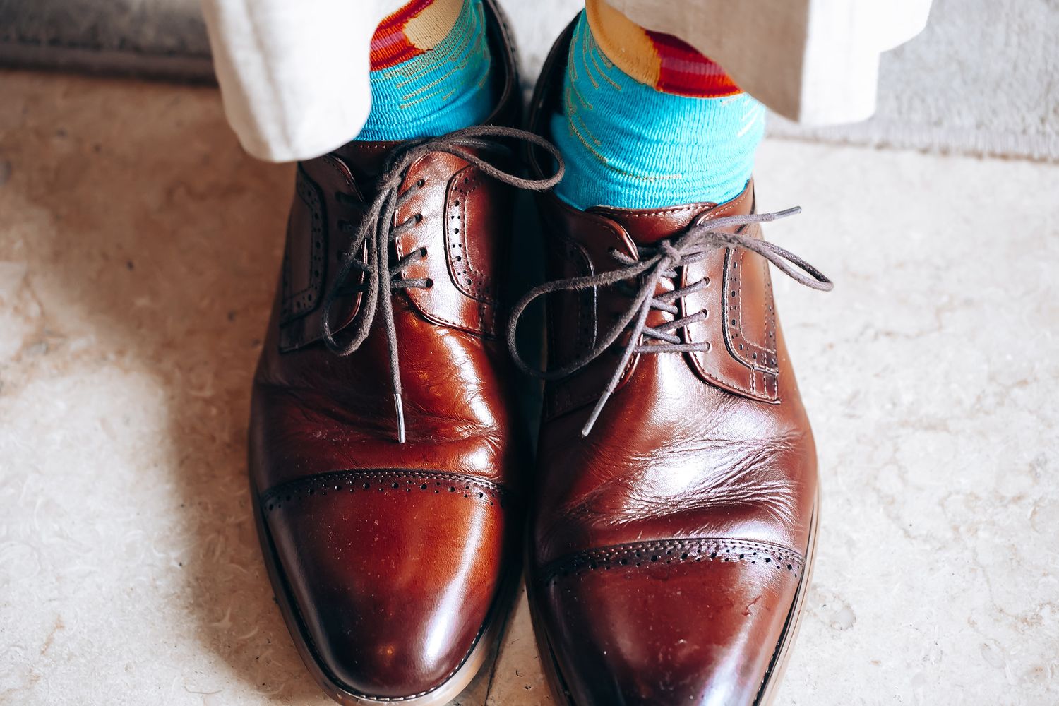 Brown leather dress shoes paired with bright turquoise socks on light flooring.