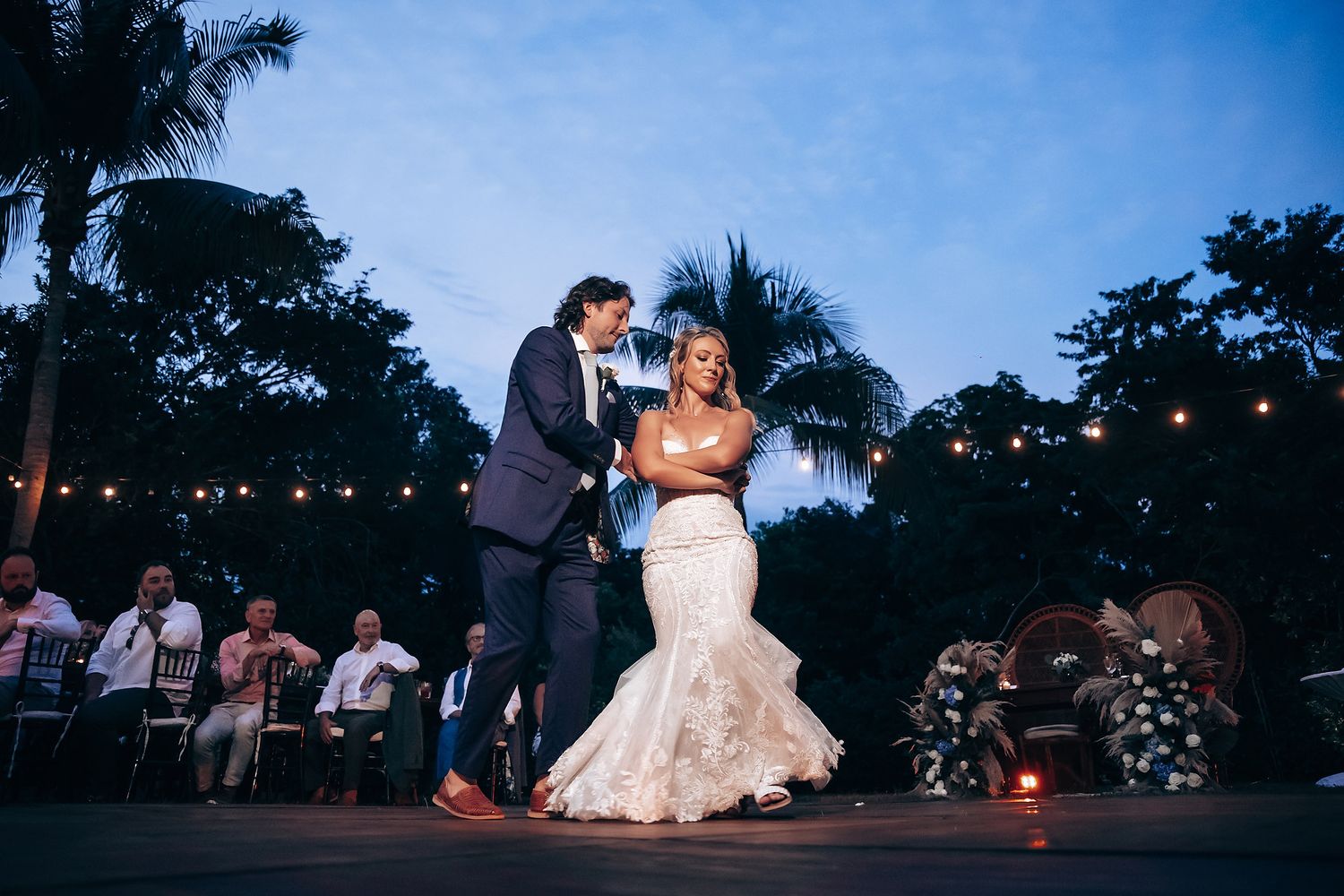 Romantic evening wedding reception with string lights illuminating couples dancing outdoors.