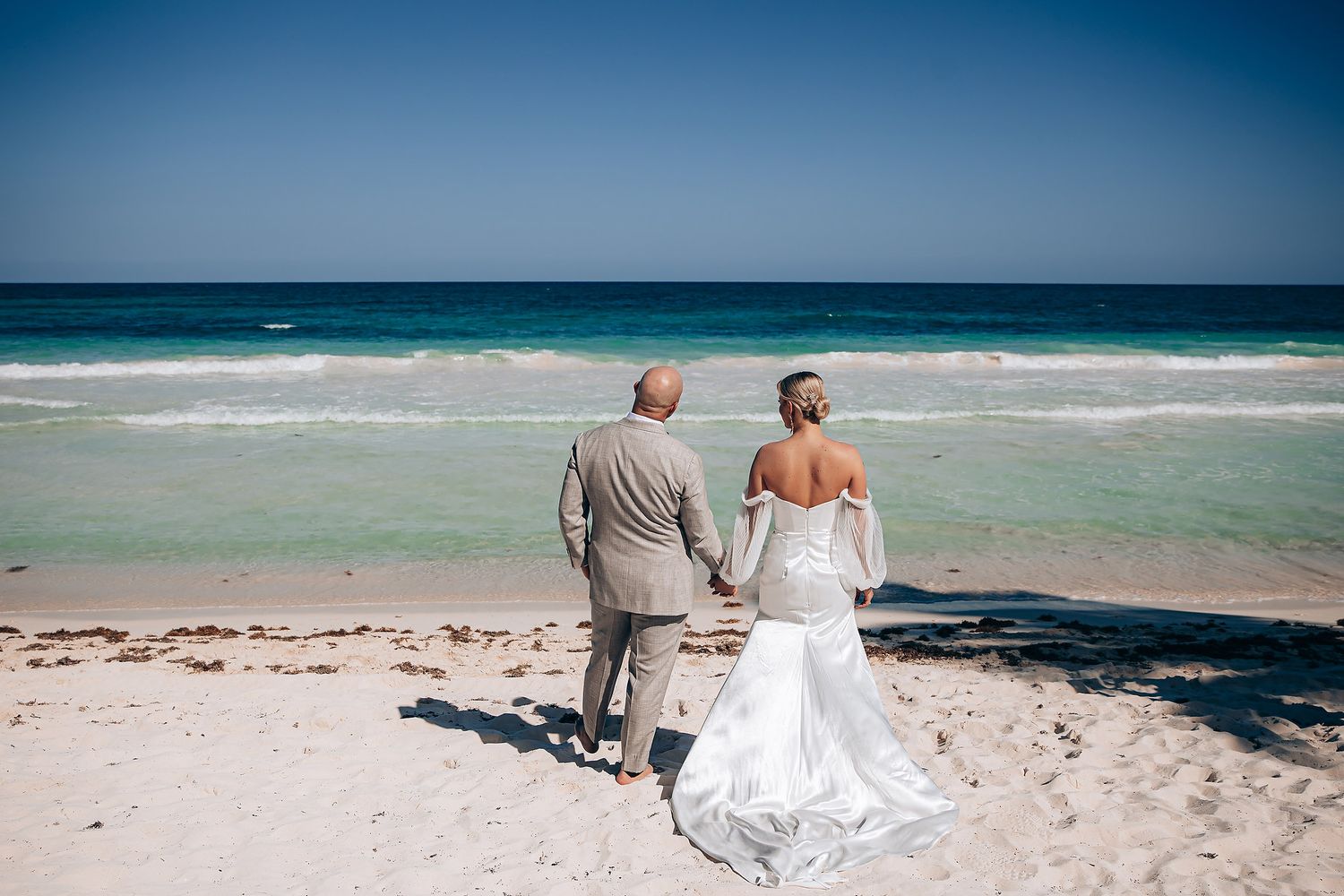 Couple walking along a pristine beach with turquoise ocean waters and clear blue sky.
