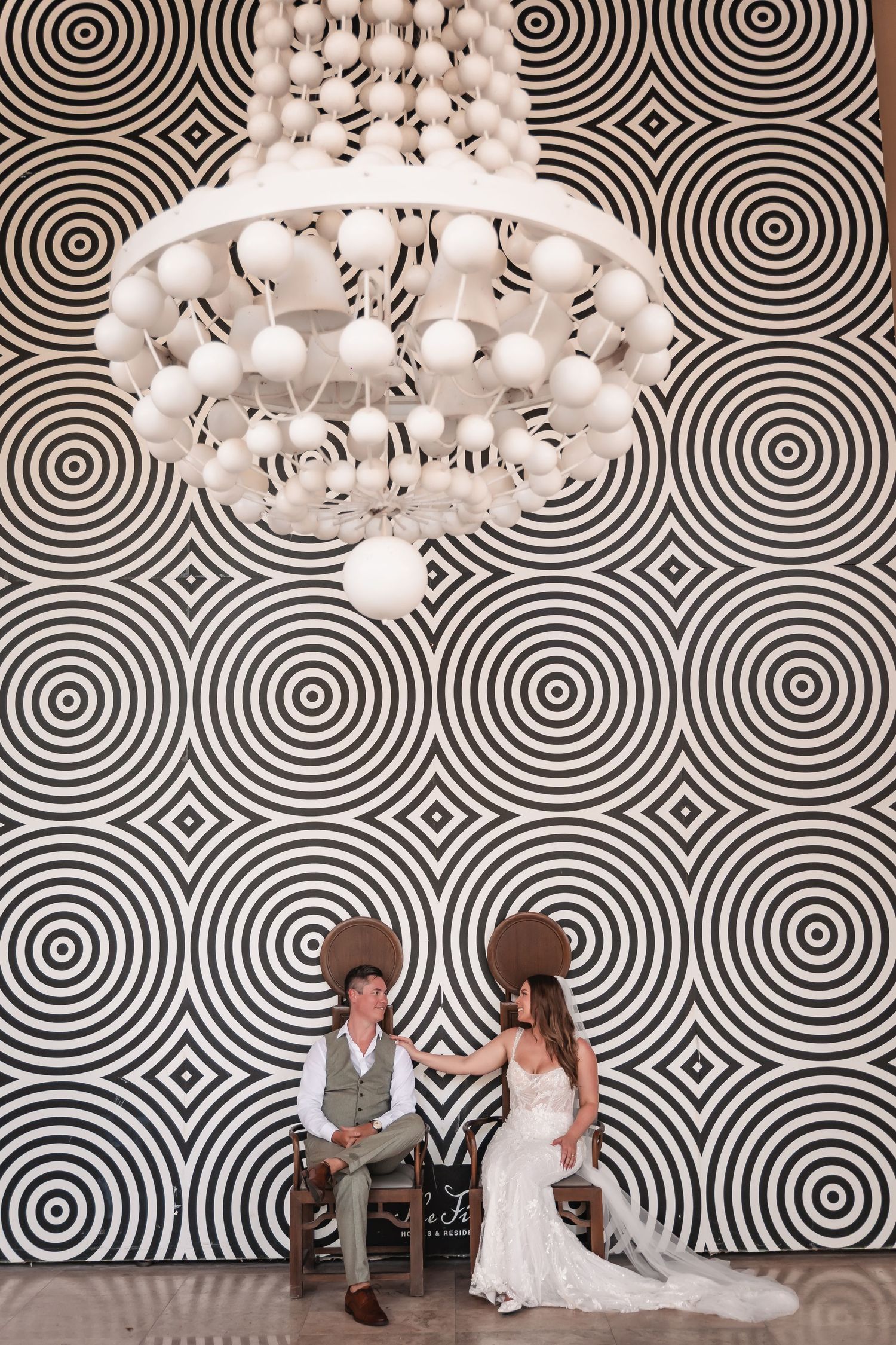 Wedding couple poses against striking black and white geometric wallpaper with modern pendant lights.