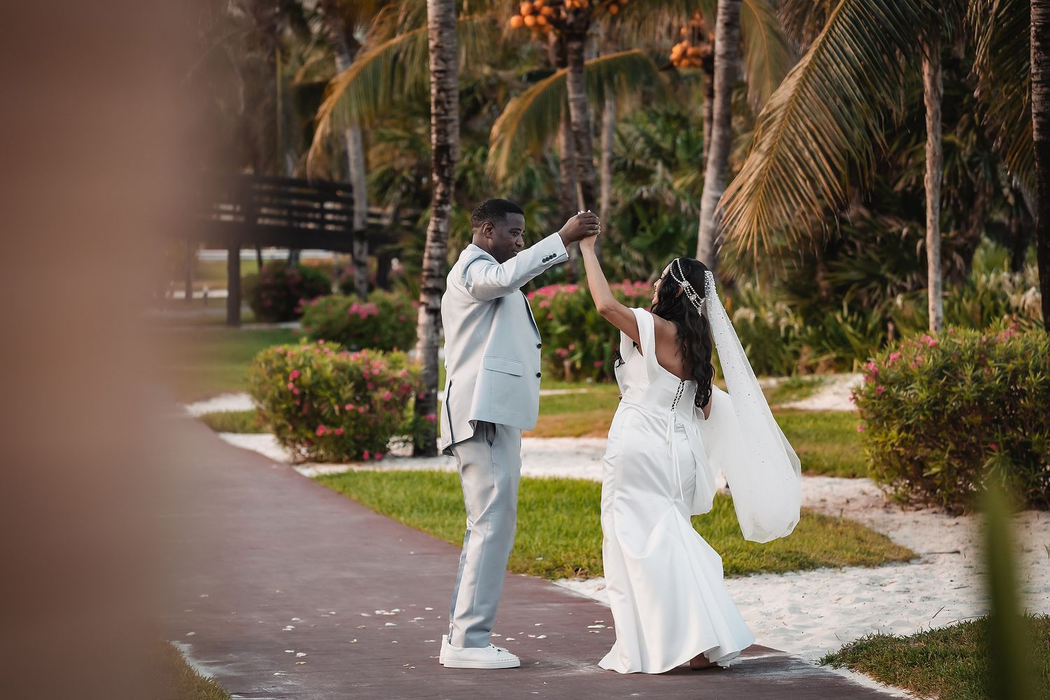 A couple walking through a palm tree-lined path in wedding attire.