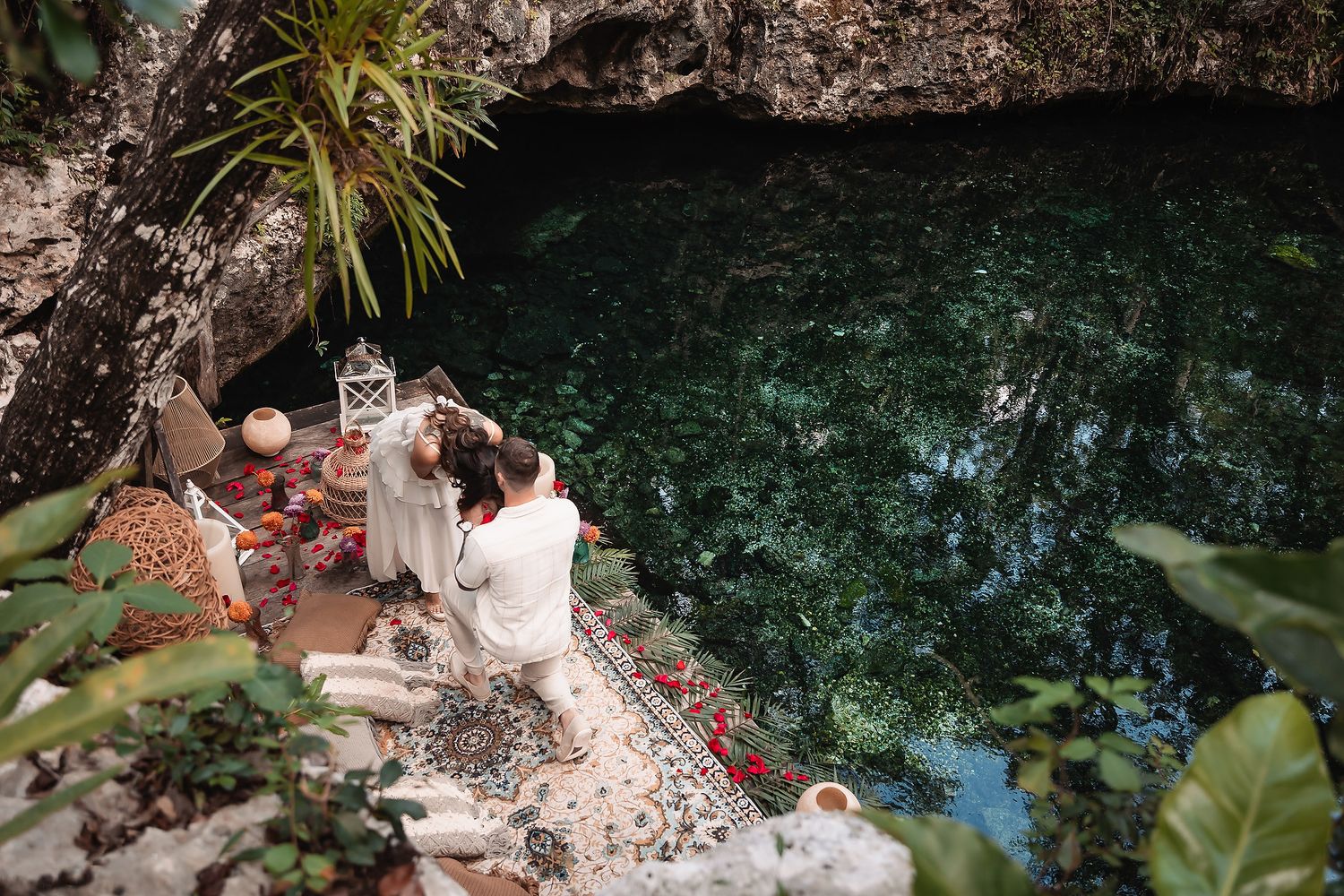 Intimate proposal scene set up beside turquoise water with decorative elements and flowers.