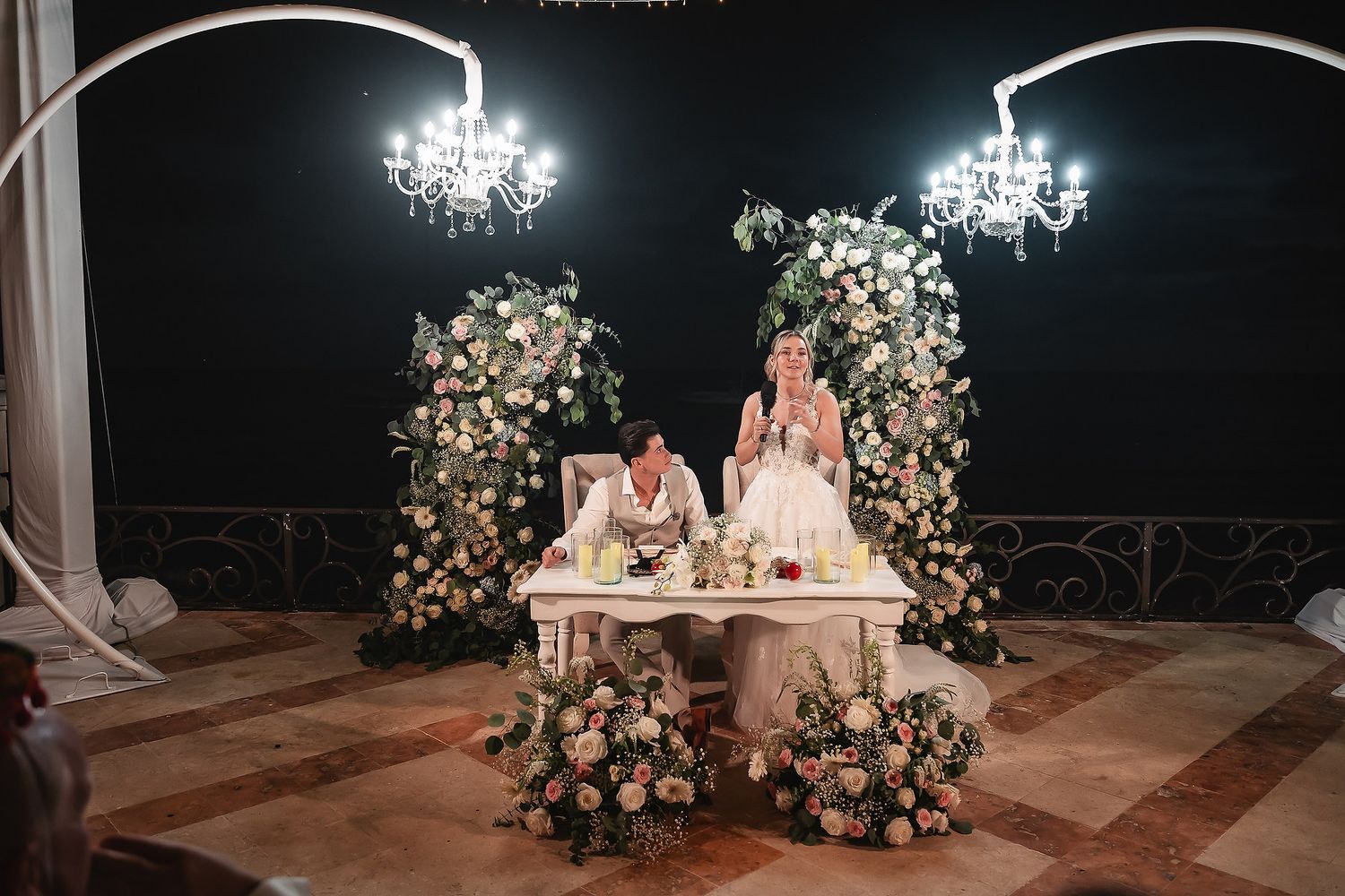 Elegant nighttime wedding reception setup with chandeliers and floral arrangements.