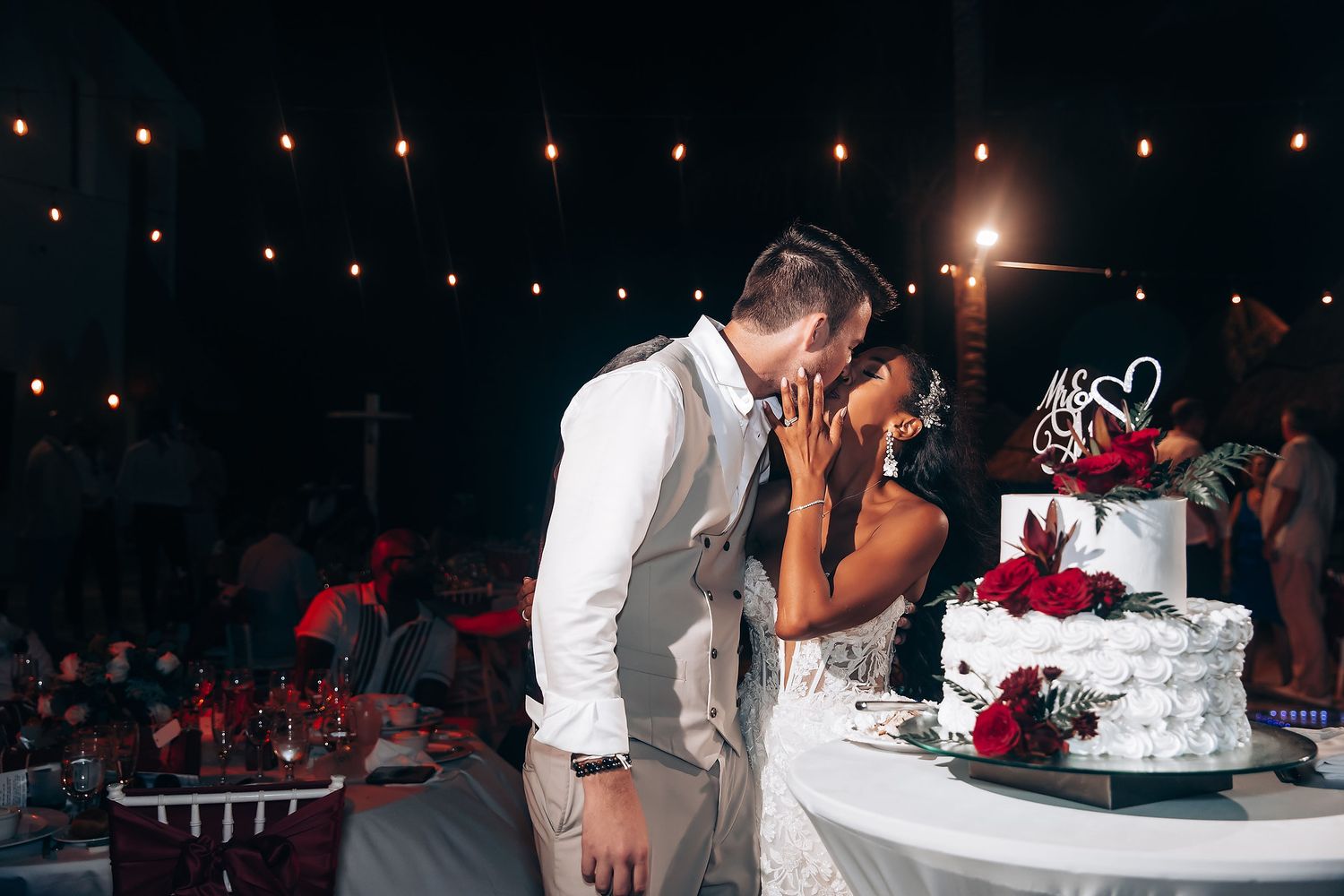Wedding cake cutting ceremony under string lights at an evening reception.
