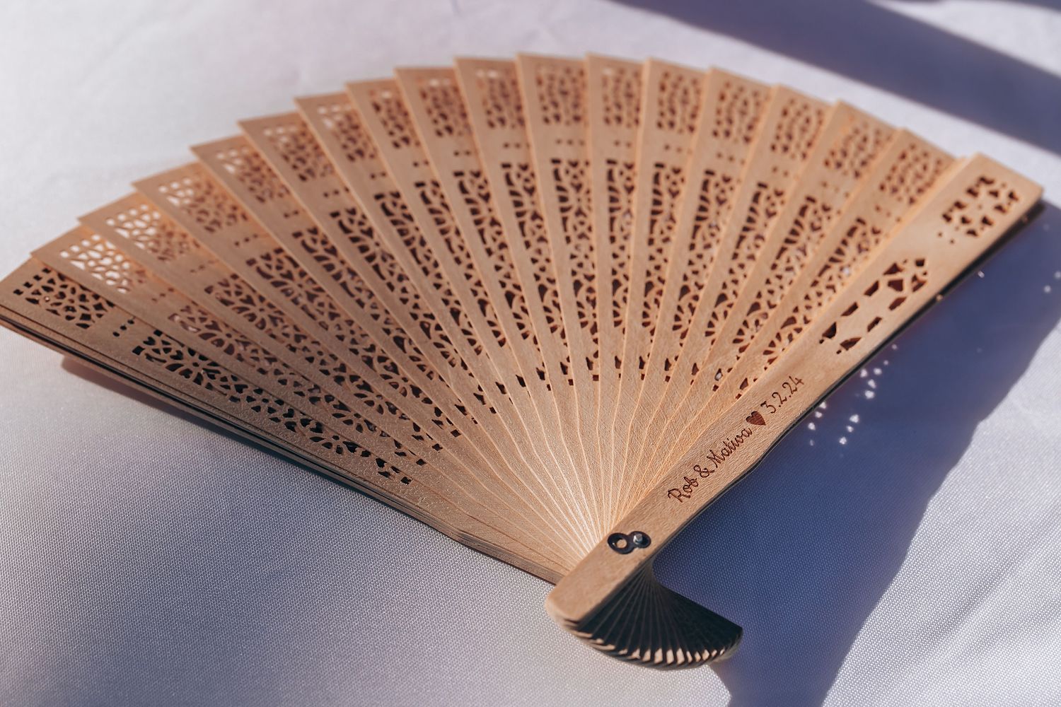 Decorative wooden folding fan with intricate carved patterns on white surface.