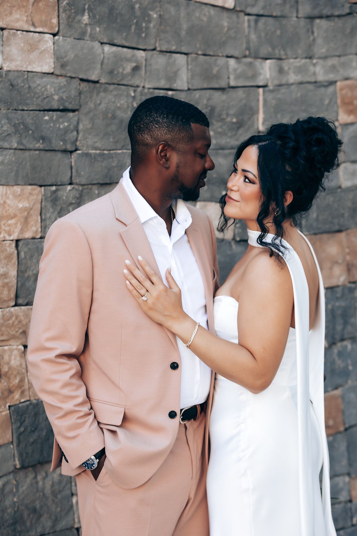 A romantic couple shares an intimate moment against a stone wall backdrop.