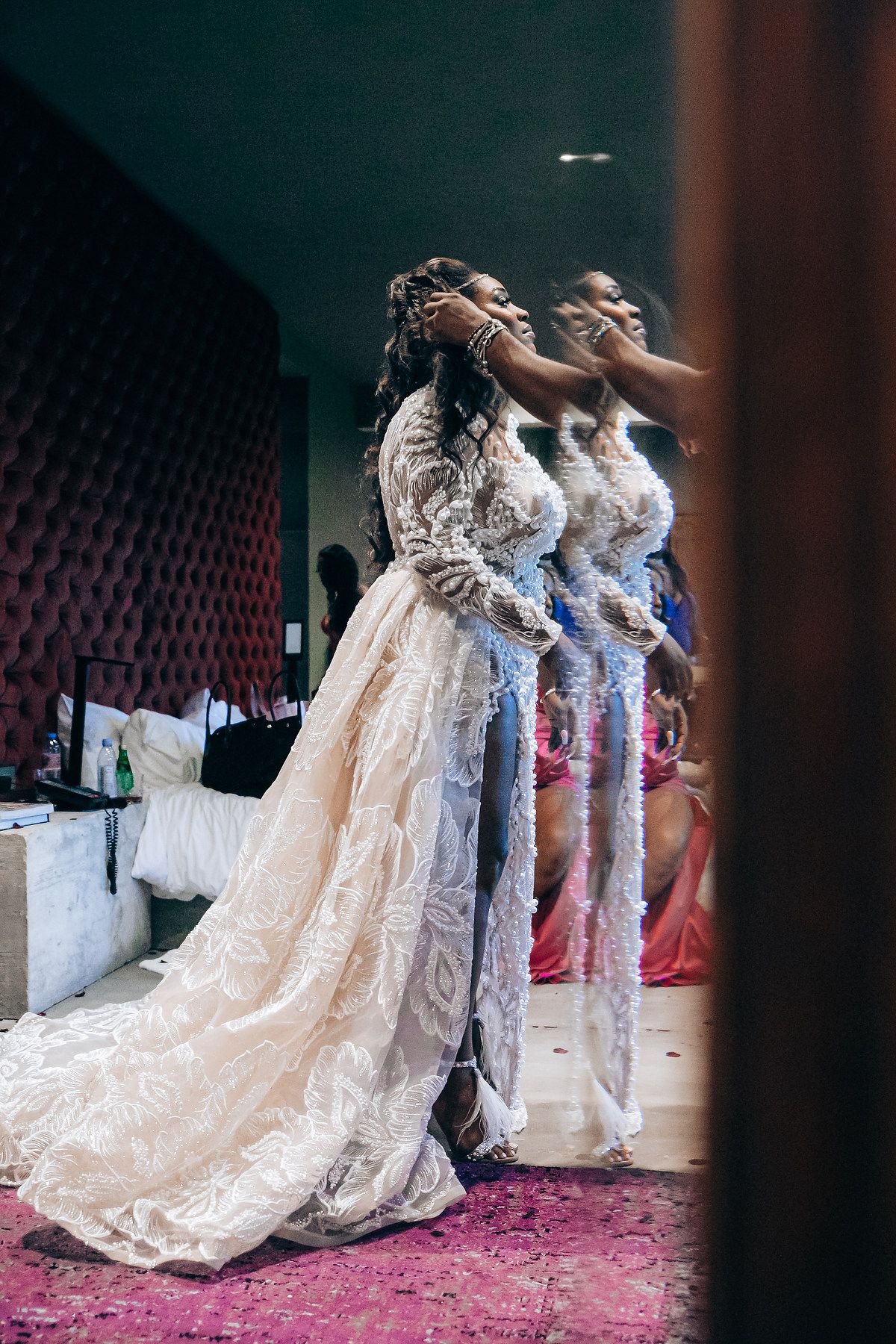 Three women in elegant lace wedding gowns stand together during a bridal celebration on a pink carpeted floor.