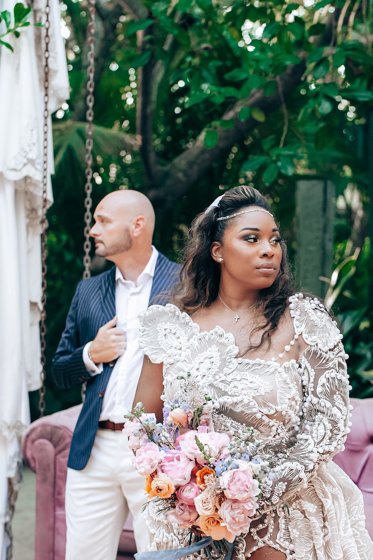 Elegant wedding scene with lace details, pink floral bouquets, and white draped decor against lush greenery.