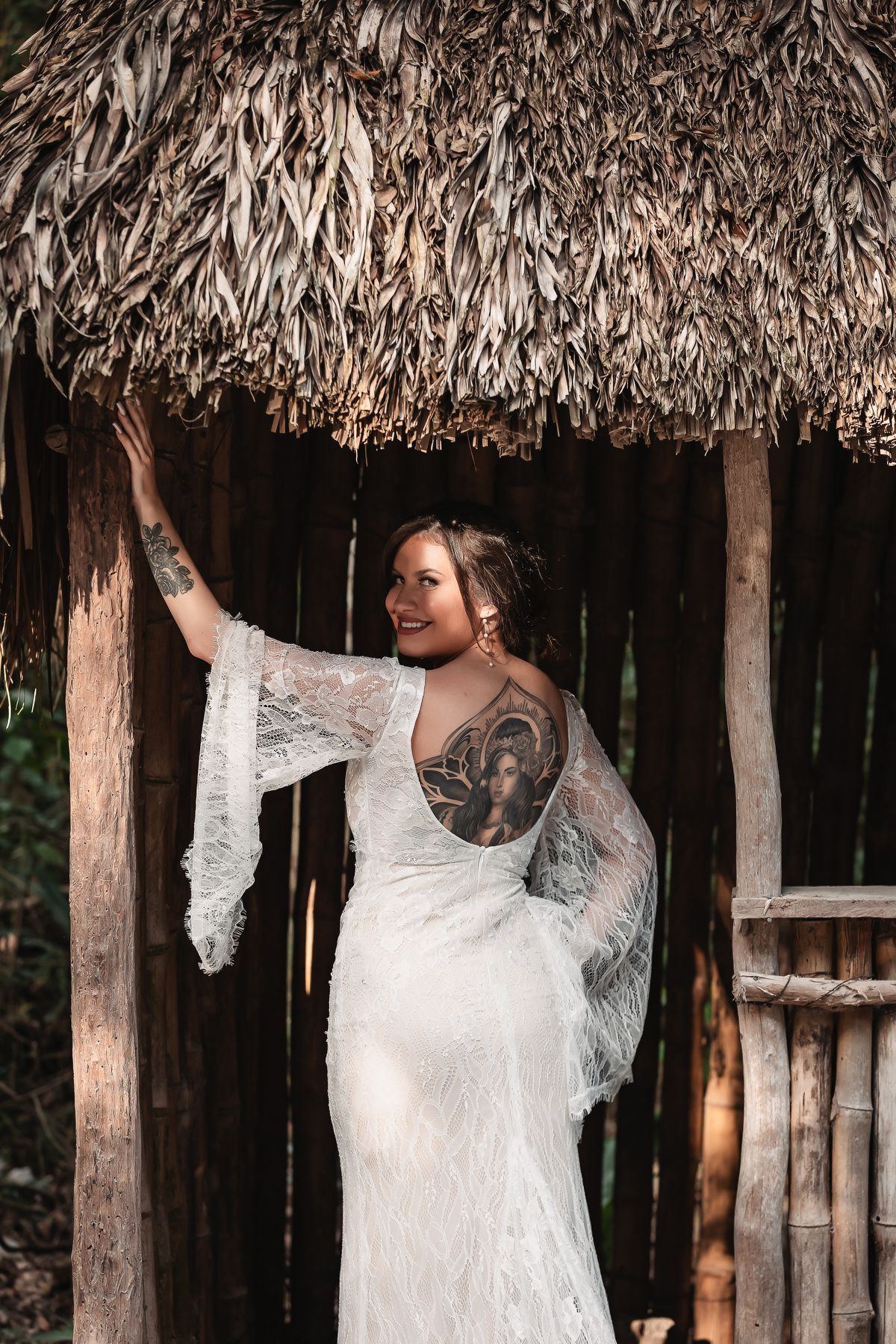A beautiful white lace wedding dress with flowing sleeves photographed under a thatched roof palapa.
