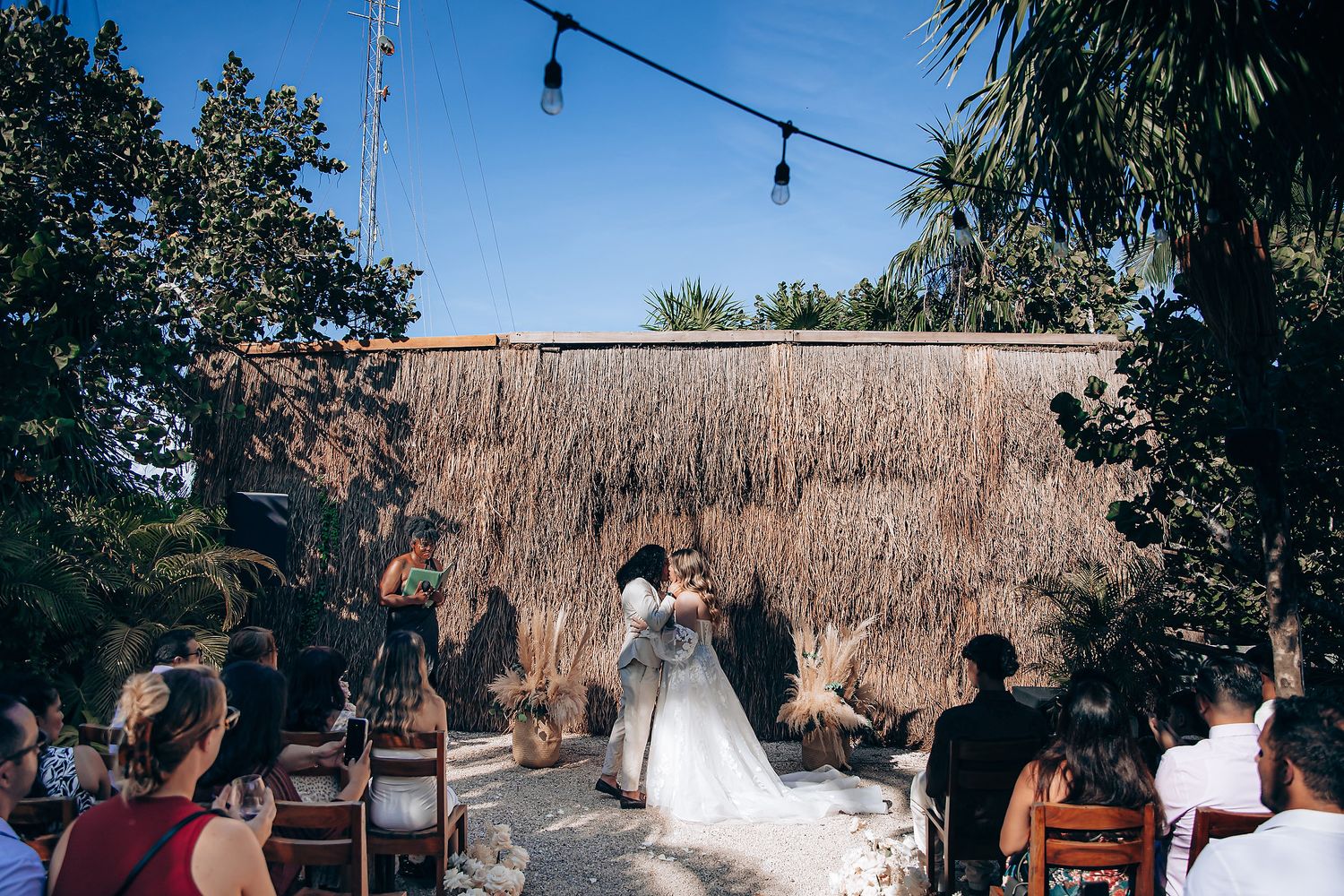 Wedding guests gather outdoors under string lights and natural decor for a rustic outdoor ceremony.
