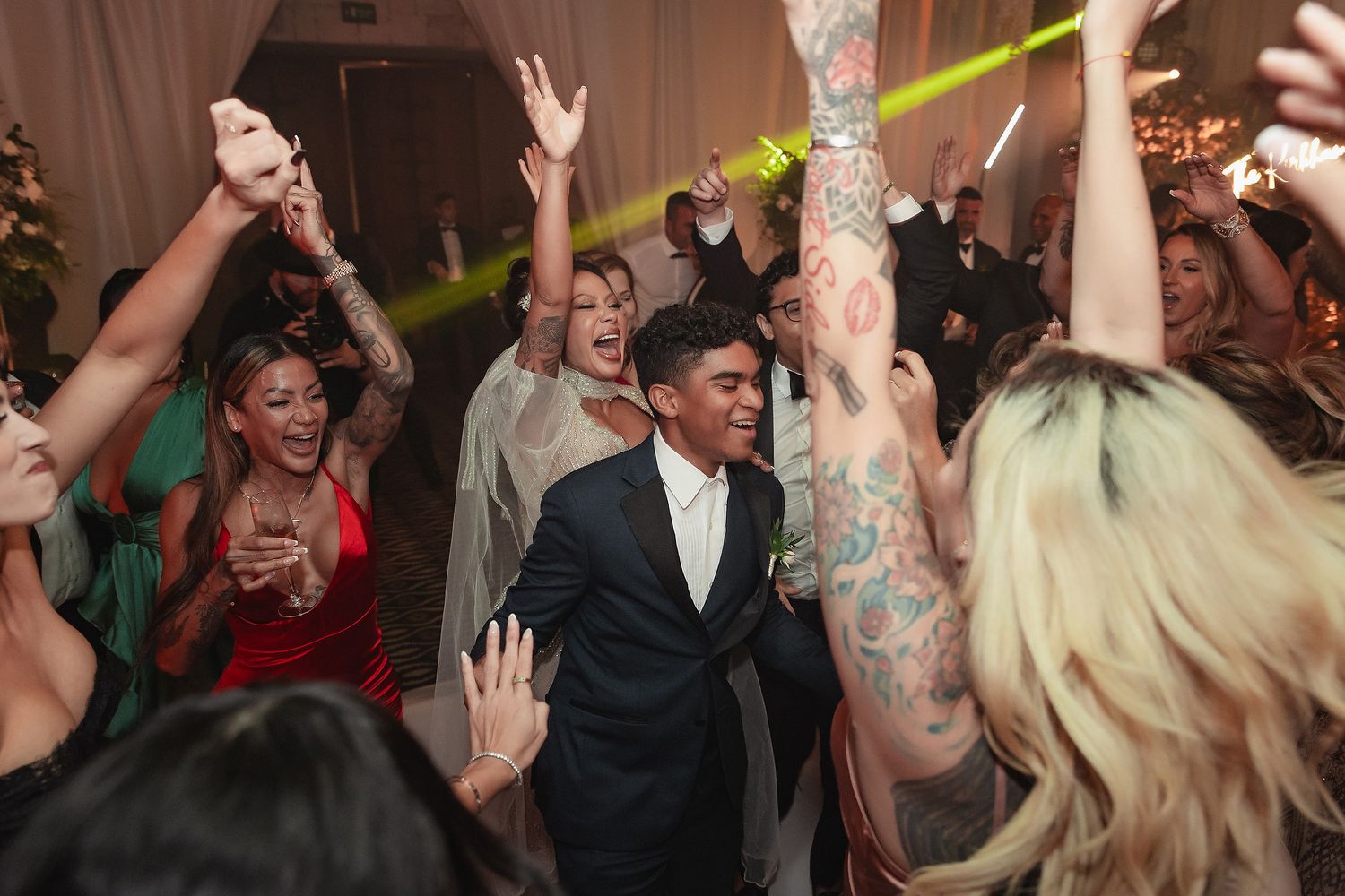 Wedding guests dance and celebrate on a crowded dance floor during a lively reception party.