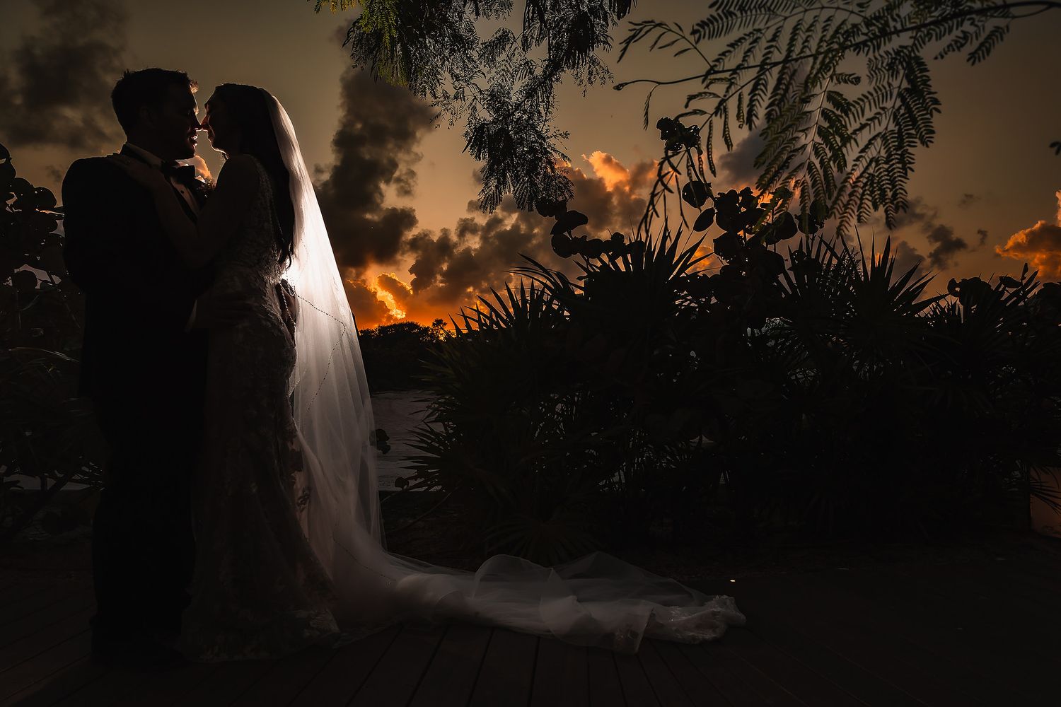 Dramatic sunset silhouettes against palm trees at a tropical wedding venue.