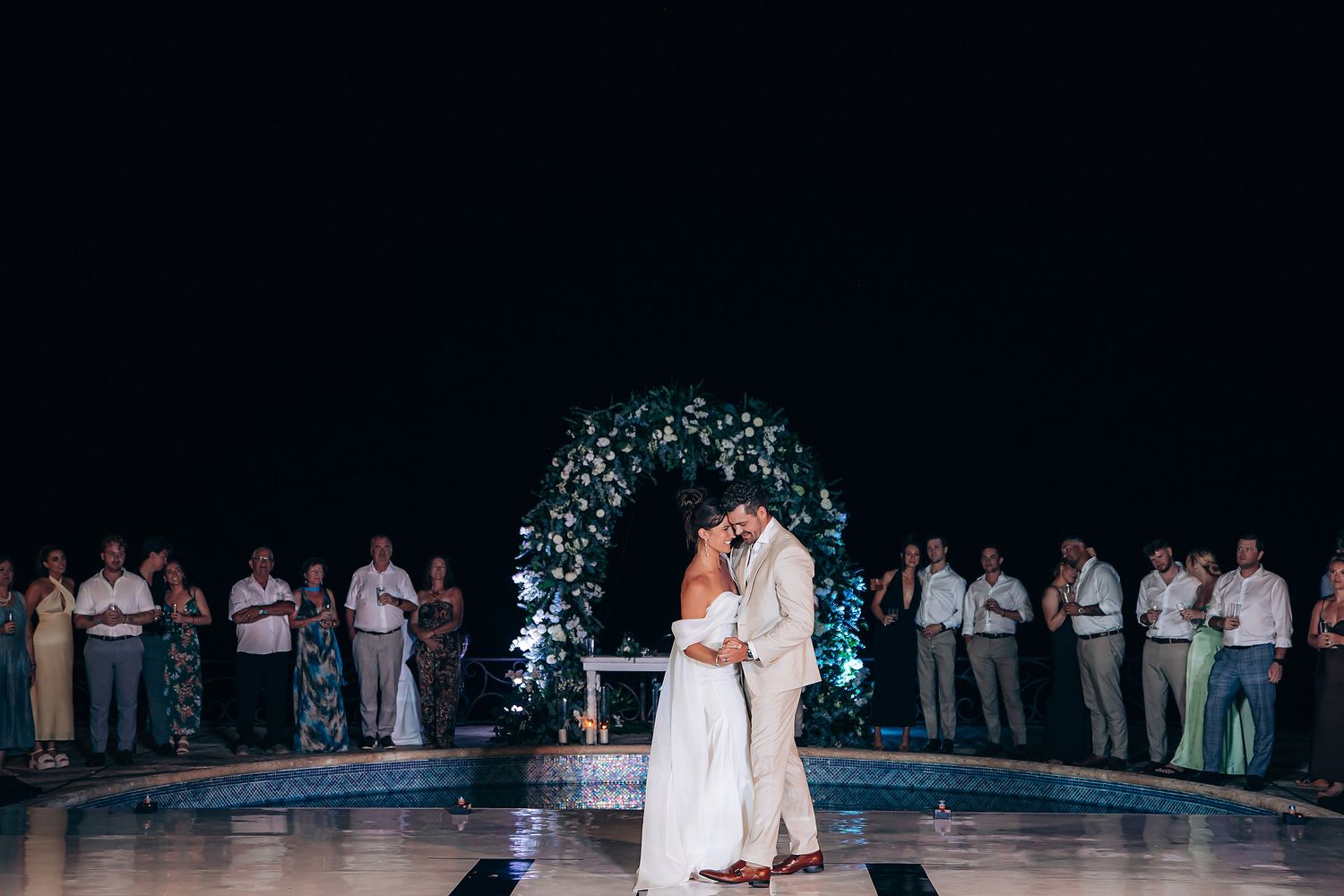 A couple shares a romantic dance at their wedding reception while guests watch from the background.