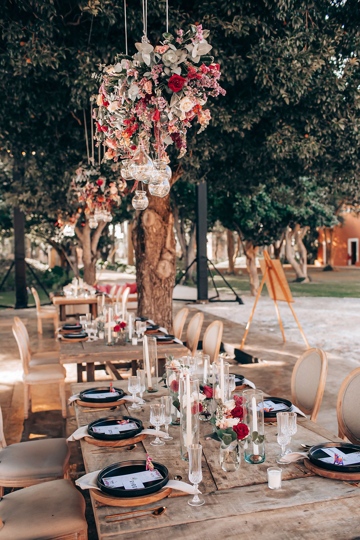 Elegant outdoor wedding reception table with pink floral arrangements, rustic wooden details and crystal glassware.