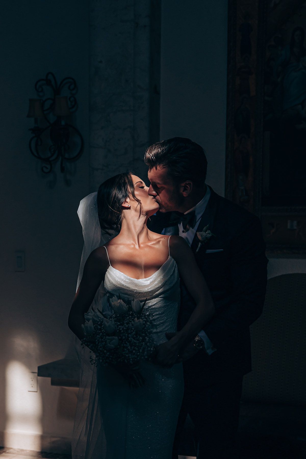 A romantic wedding couple shares an intimate dance in dramatic lighting with shadows and highlights creating a moody atmosphere.