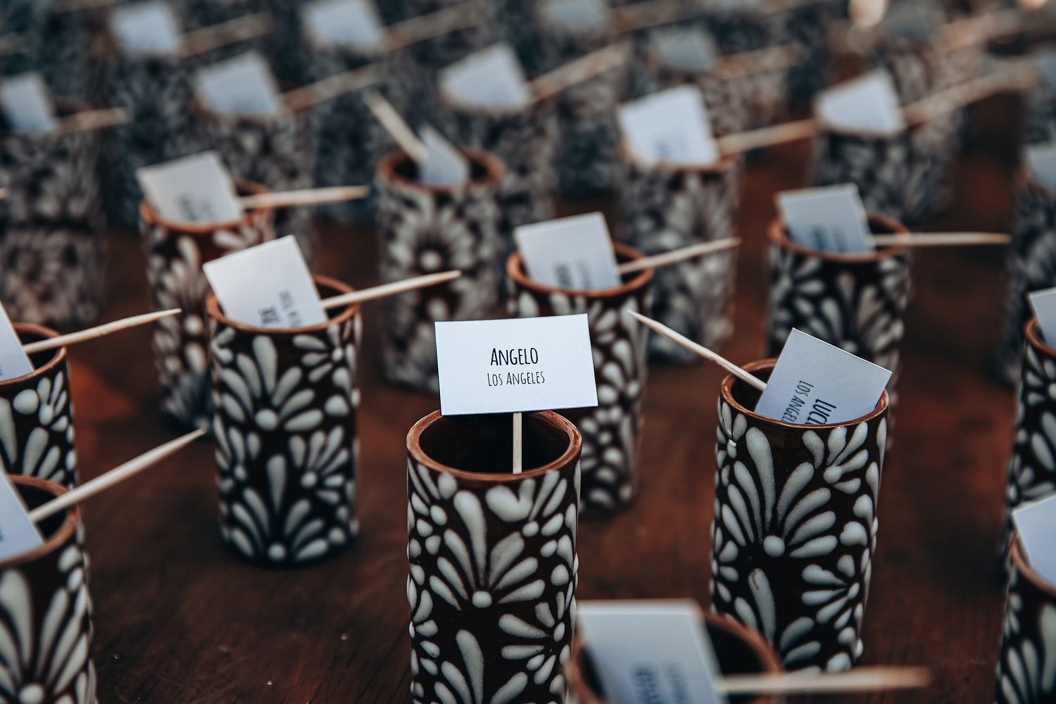 Wine bottles with black and white patterned labels line up in rows on wooden shelves in a wine cellar.