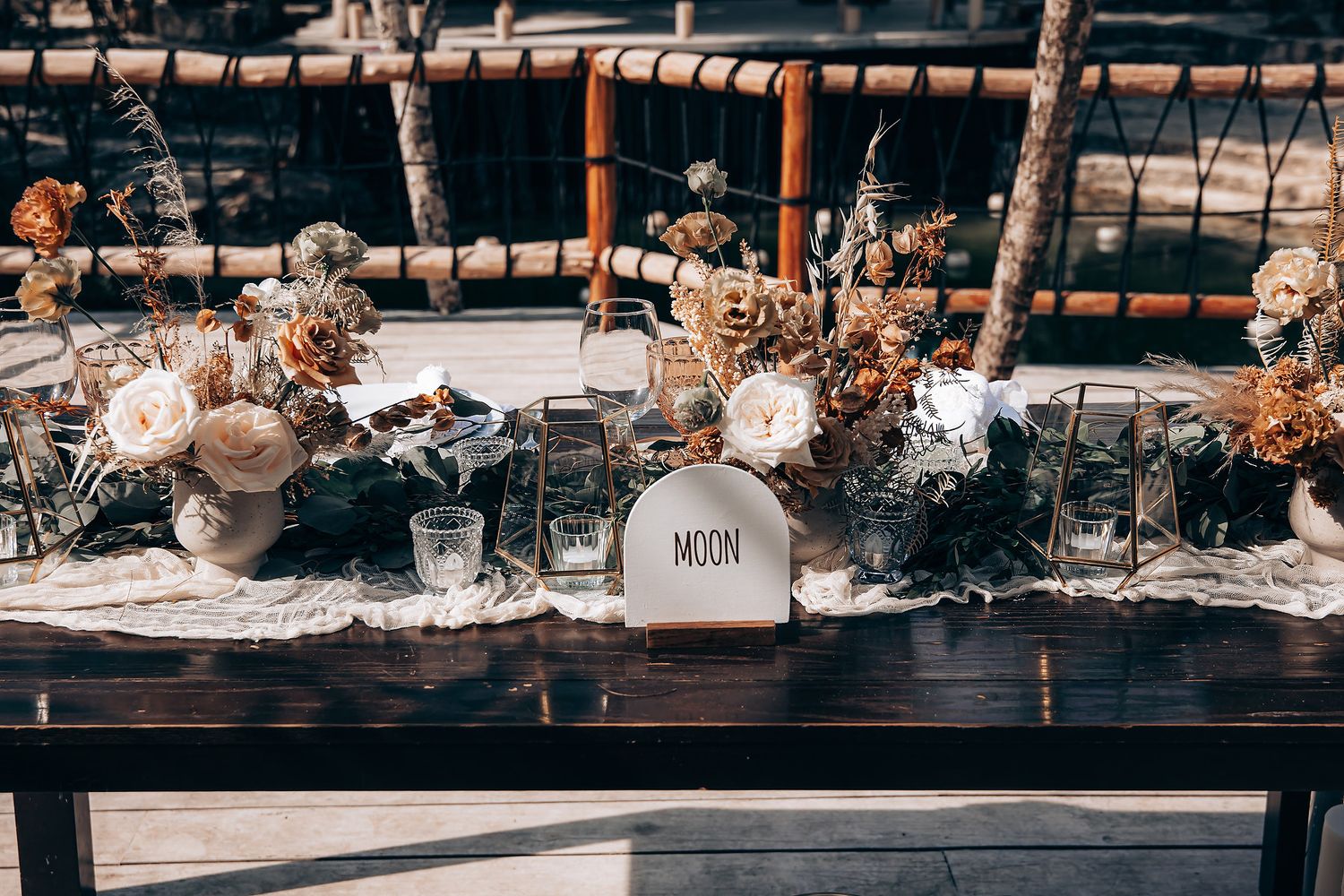 Rustic wedding table setting with vintage decor, candles and floral arrangements on a wooden surface.