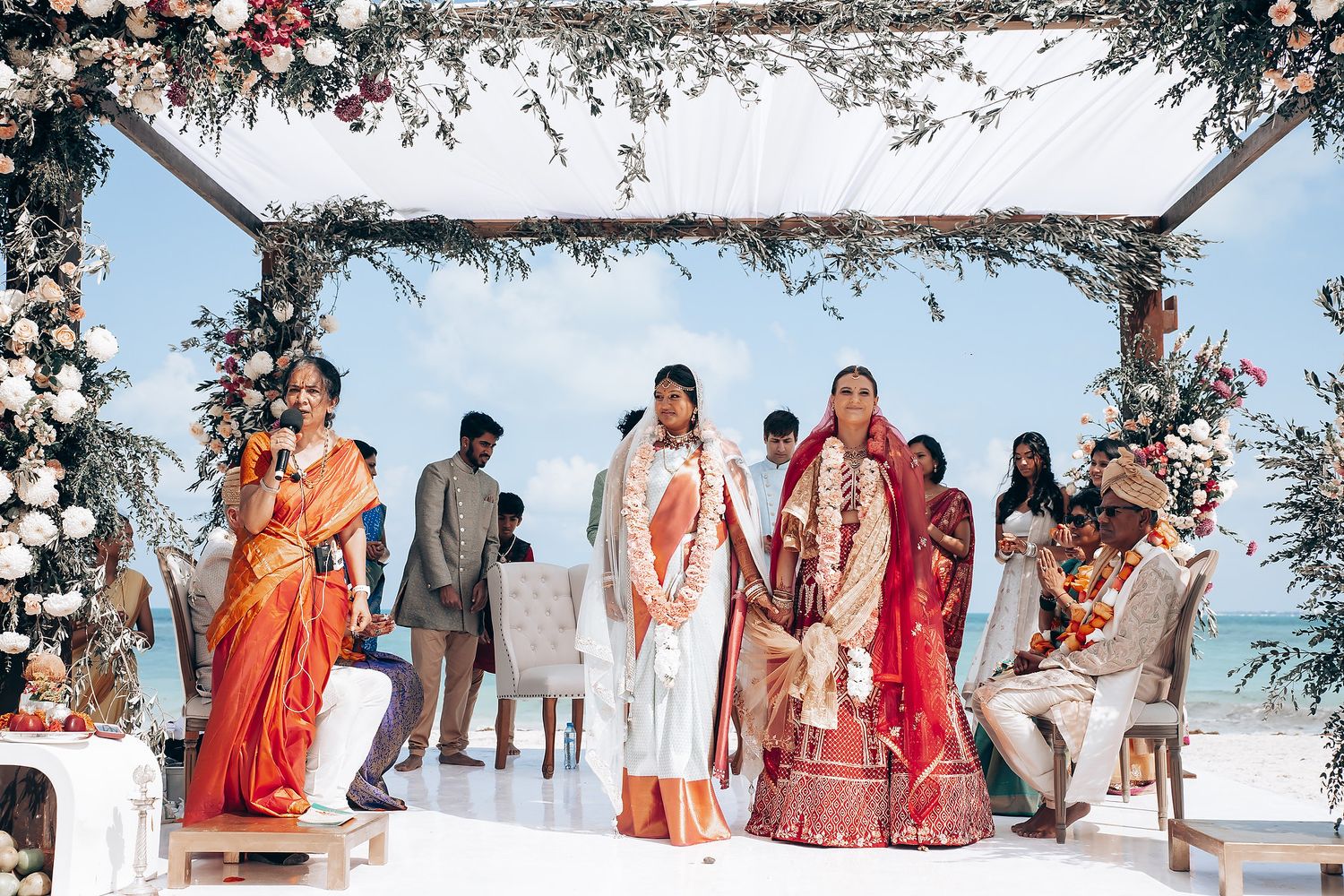 Wedding guests gathered under decorated white canopy for beachside ceremony.