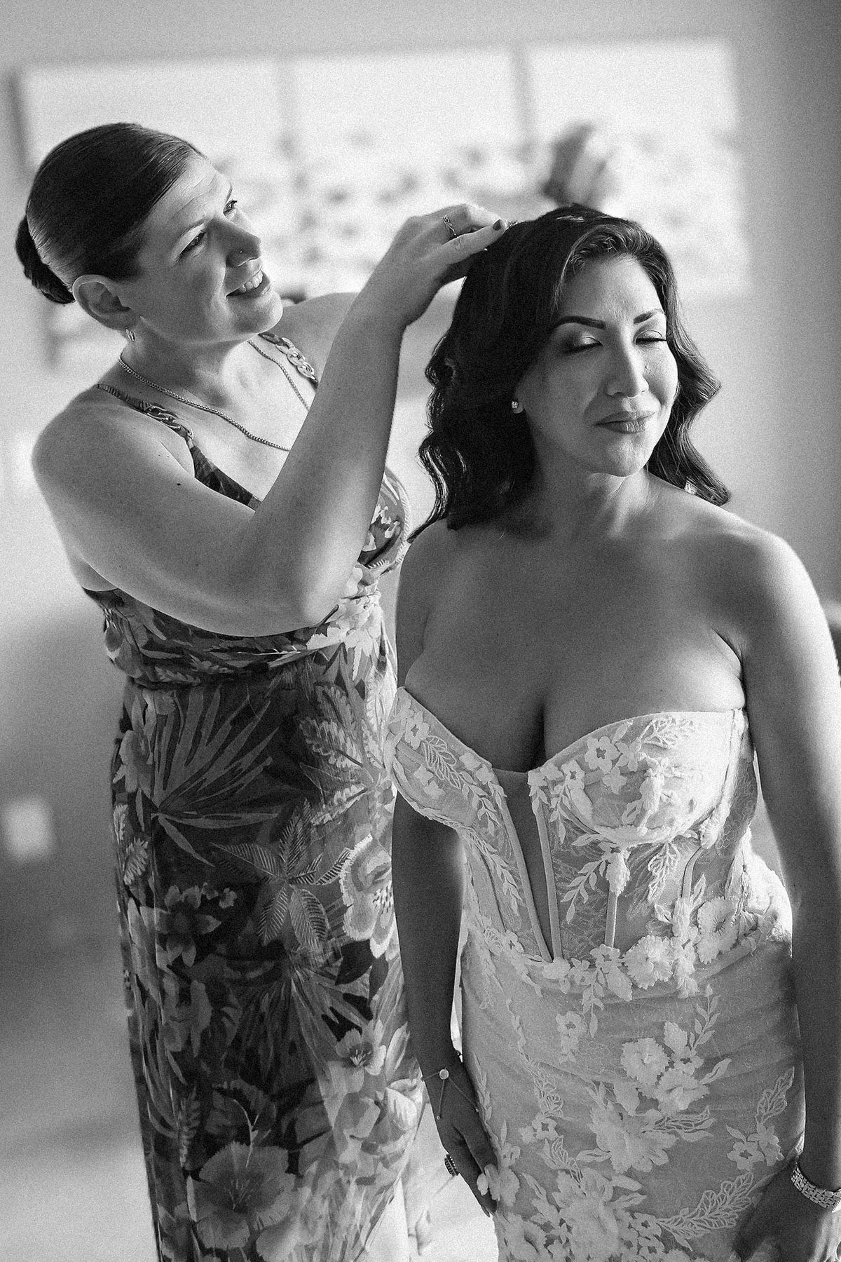 Black and white photo of a bridesmaid helping a bride with her hair before the wedding ceremony.