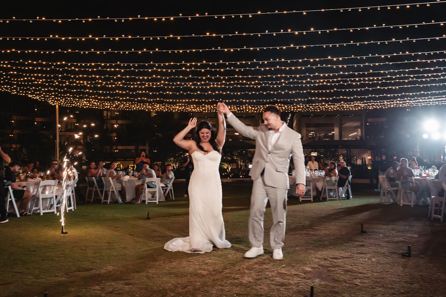 Bride and groom dance under string lights at outdoor wedding reception at night.