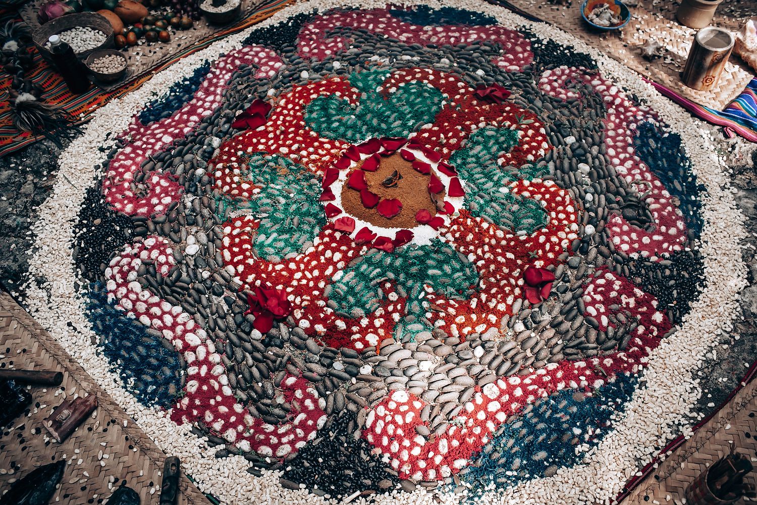 Aerial view of a vibrant floral mosaic mandala made from colorful petals and stones in red, green, and white.