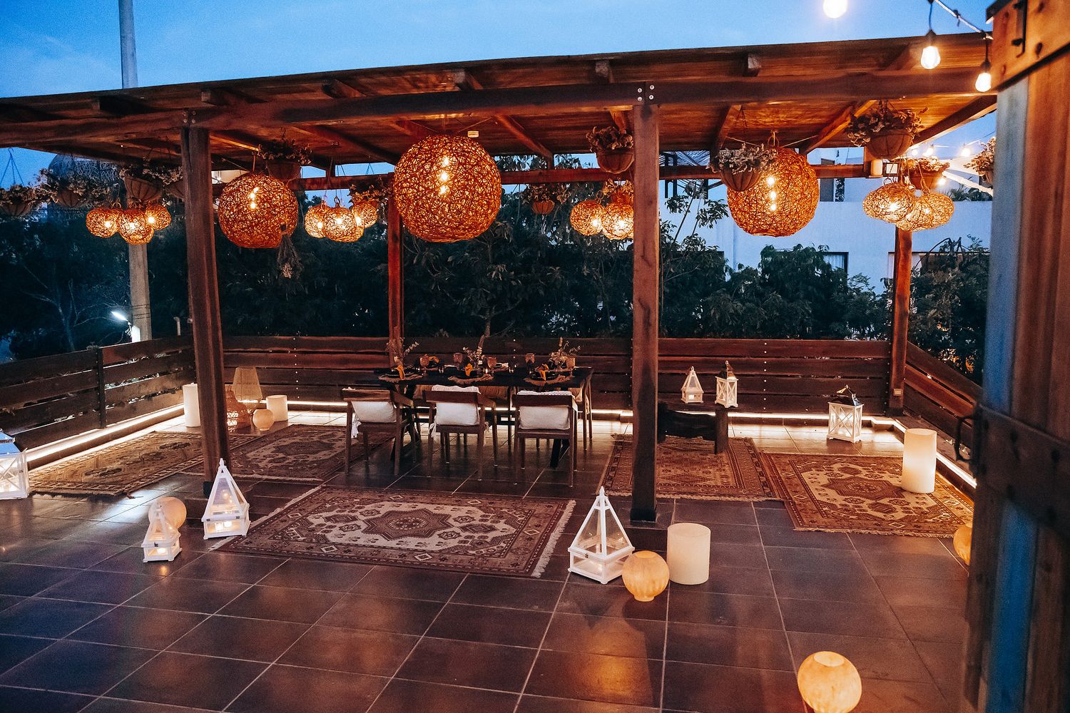 Boho outdoor wedding reception space at twilight with globe wicker lights and patterned area rugs.