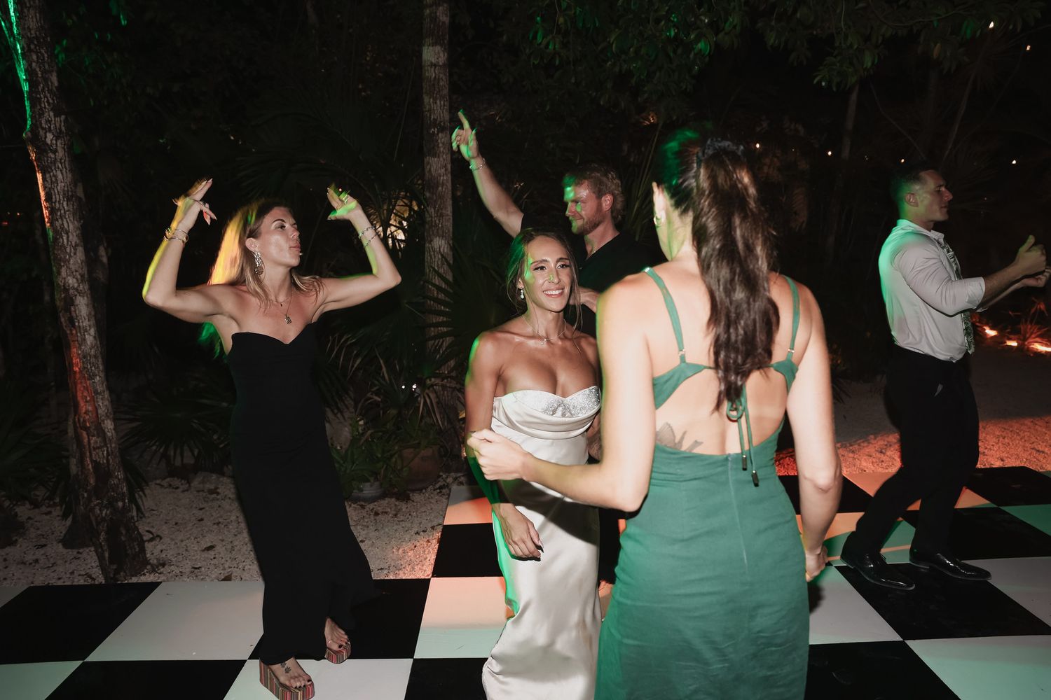 Guests dancing joyfully on a black and white checkered dance floor at an outdoor evening wedding reception.