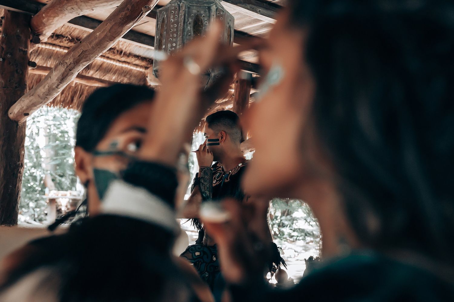 People applying traditional Mayan face paint in a rustic open-air setting during a cultural ceremony.