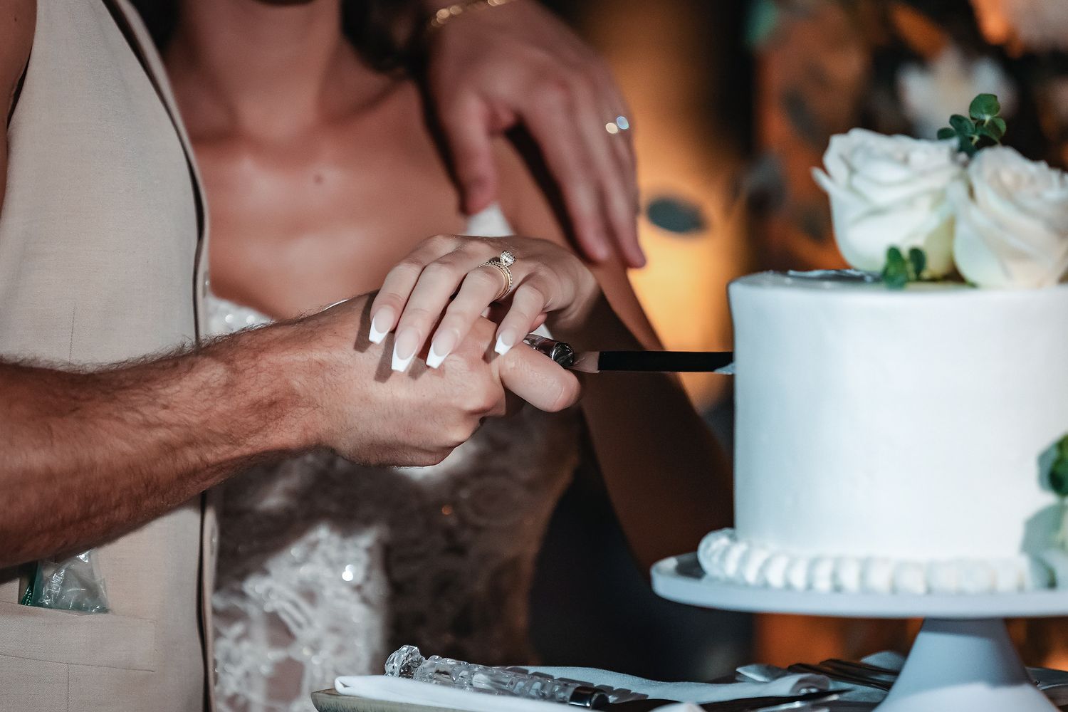 Bride and groom cutting white wedding cake decorated with roses together at their wedding reception.