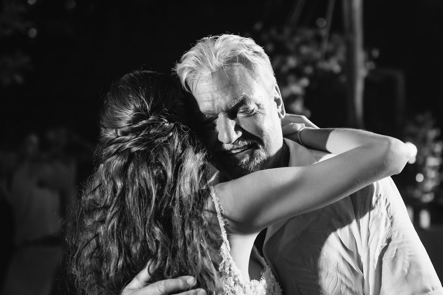 Black and white photo of an older man and young woman sharing an emotional embrace at a wedding dance.