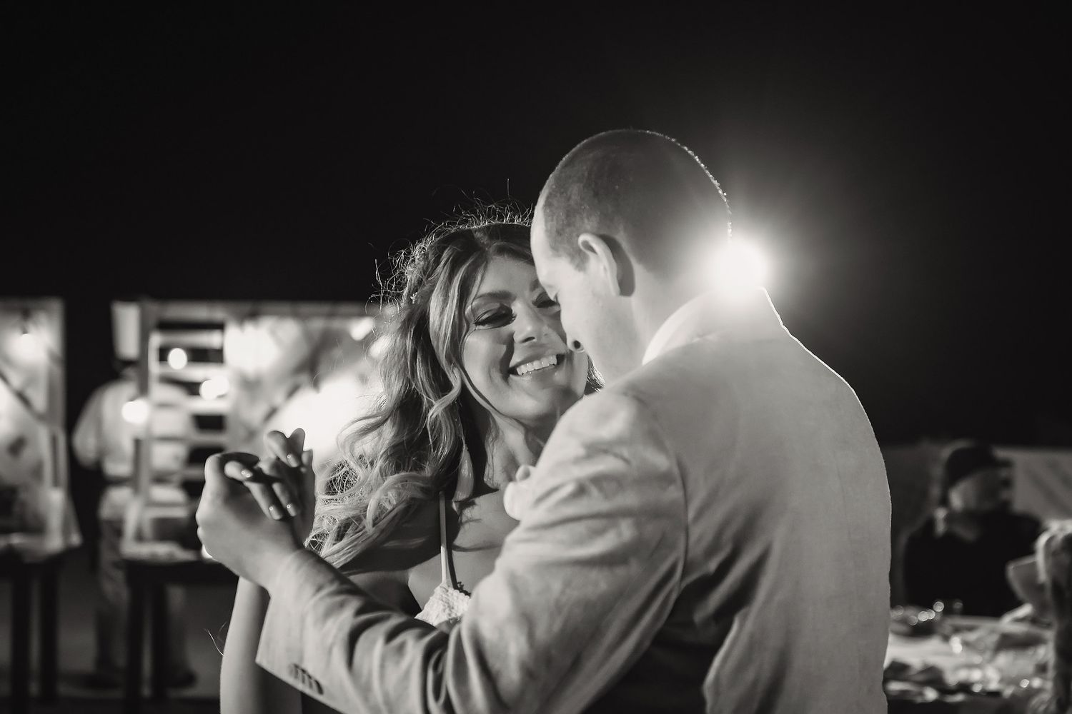Black and white photo of a smiling couple sharing a romantic dance at an outdoor evening event.