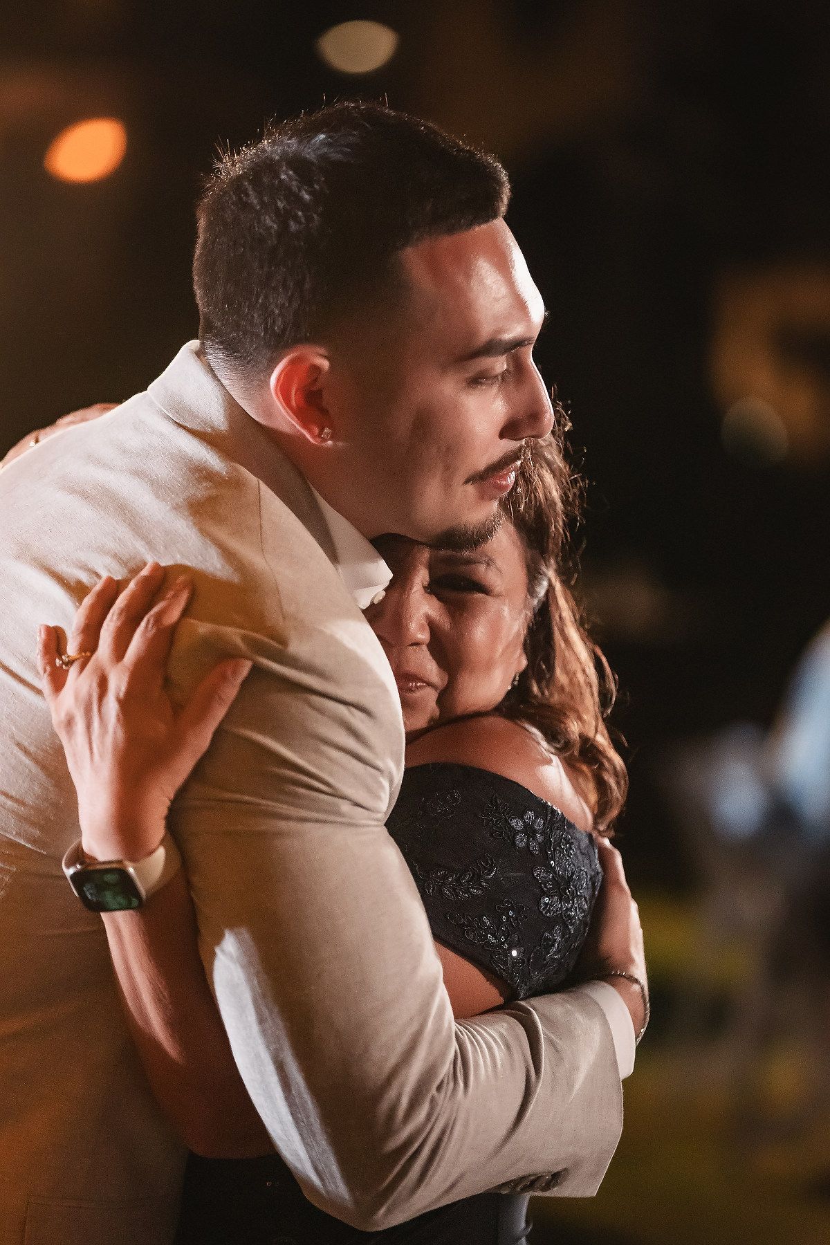 A young couple shares a tender embrace outdoors at night, with the man in a suit hugging a woman in a dark dress.