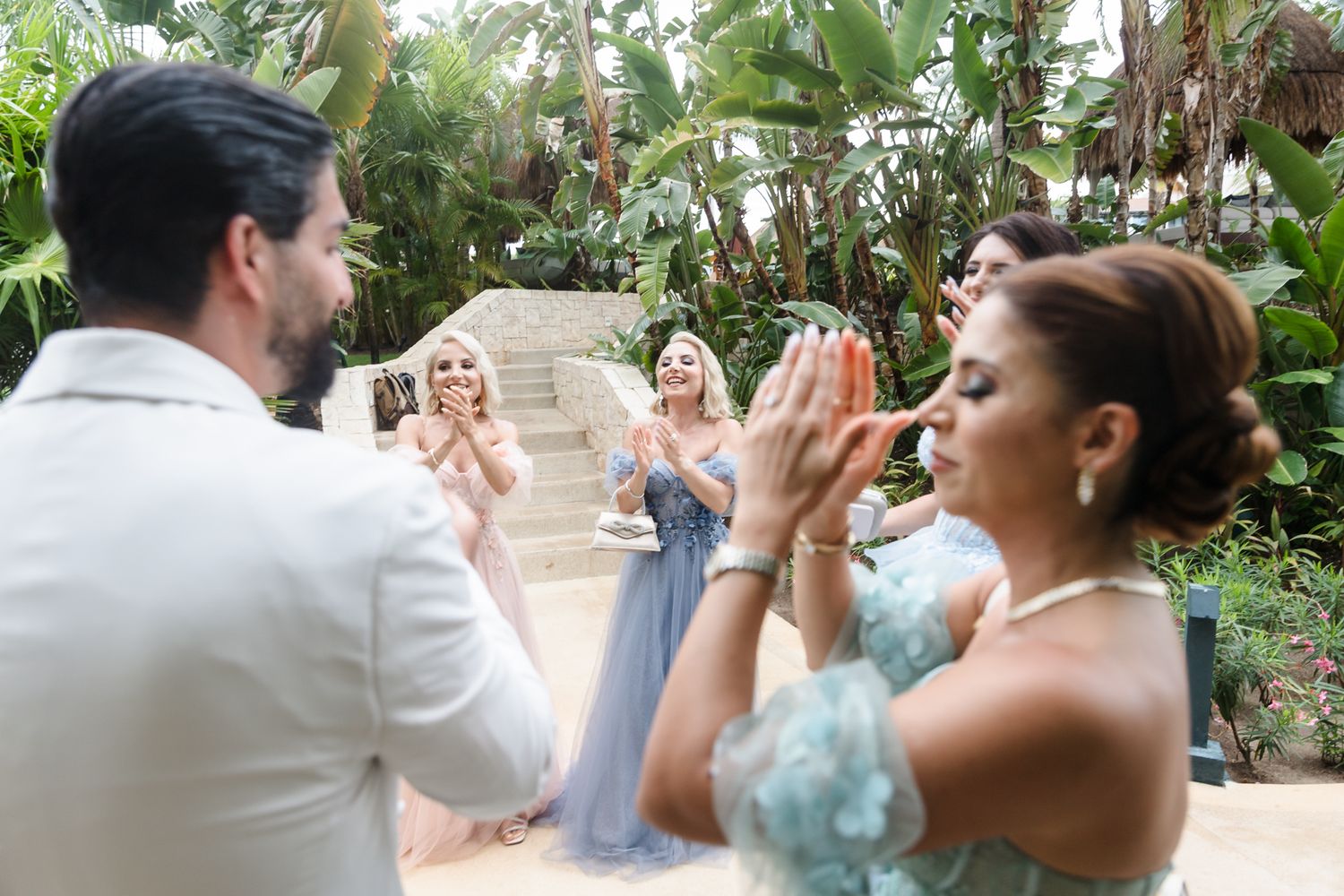 Guests clapping and celebrating with groom at outdoor tropical wedding ceremony.