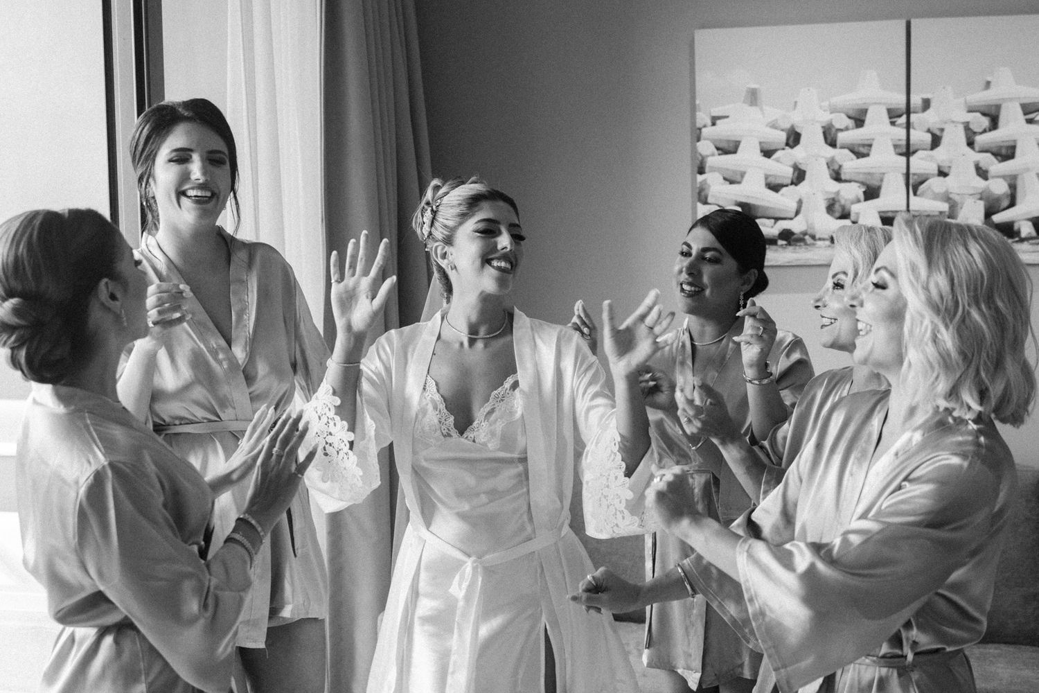 Black and white photo of bride and bridesmaids in robes laughing and celebrating on wedding morning.